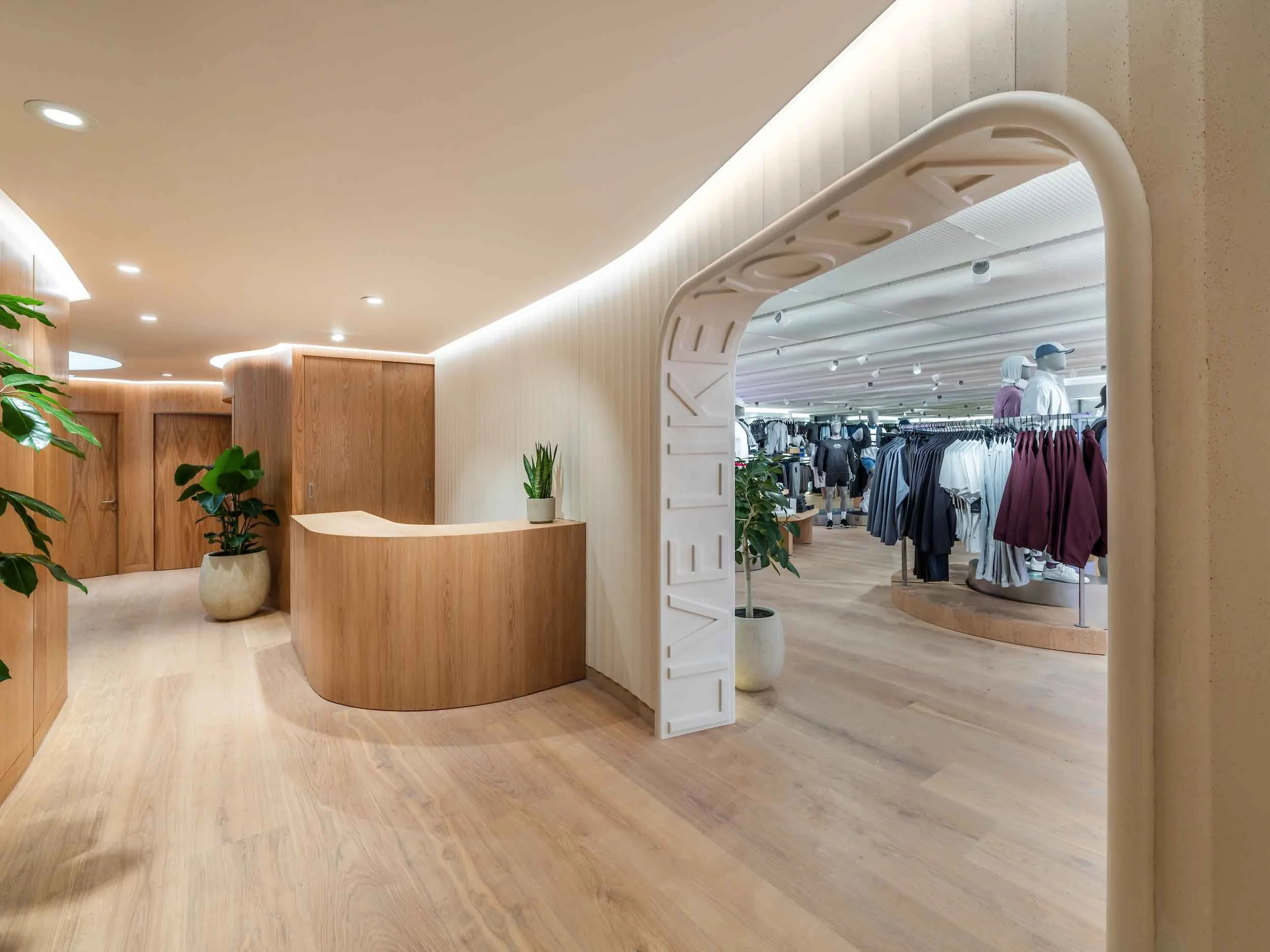 Interior of a clothing store with wooden floors and walls, a curved white decorative archway, and mannequins wearing casual clothing.