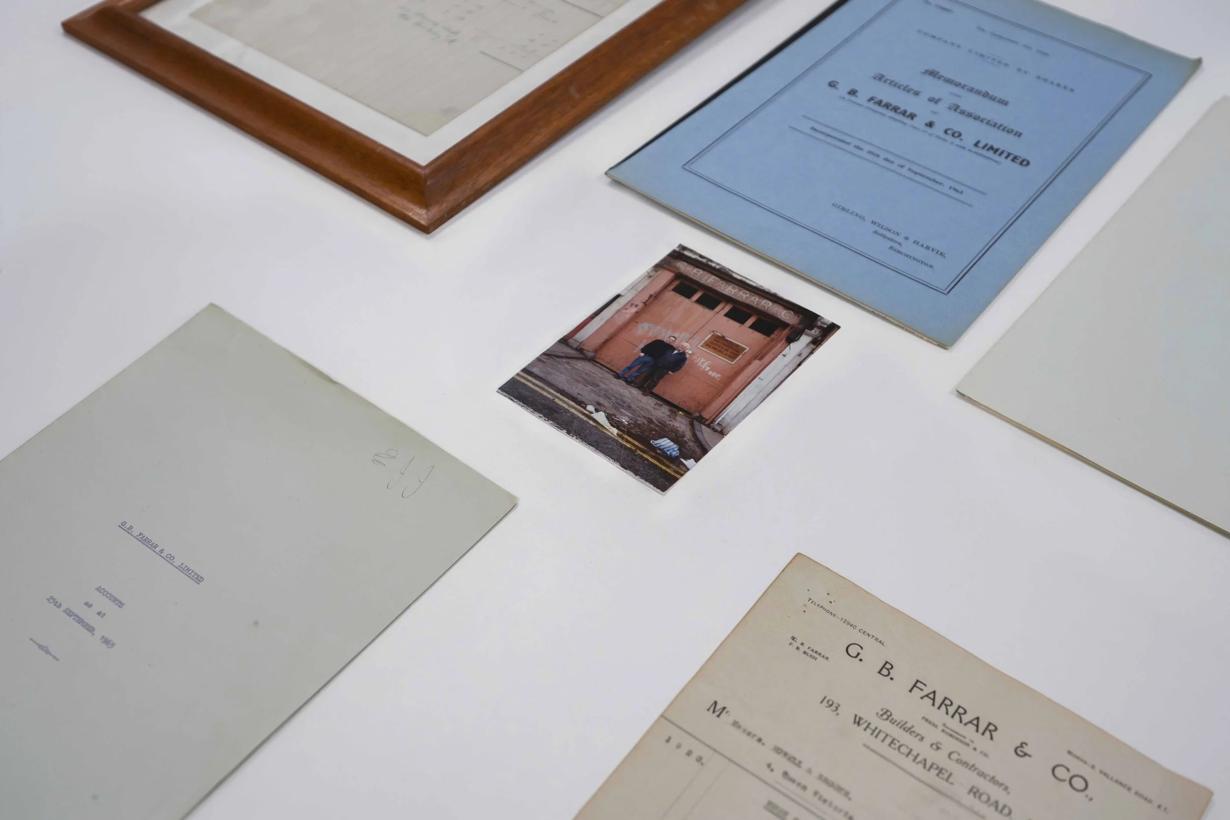 Collection of old documents, blueprints, and a photograph displayed on a flat surface, with some documents including a certificate or official paper from G. B. Farrar & Co. Limited and other papers of varying colors and sizes.