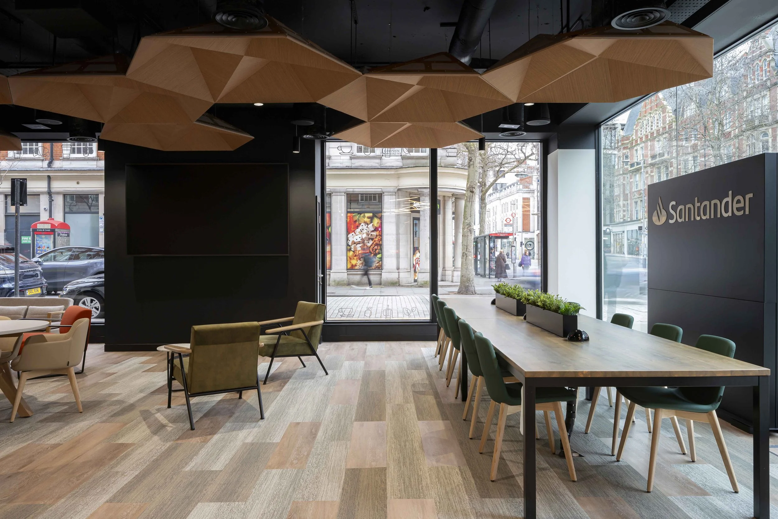 Interior of a modern bank branch with a large window, wooden ceiling panels, and seating area. Outside, city street with cars, pedestrians, and historic buildings visible.