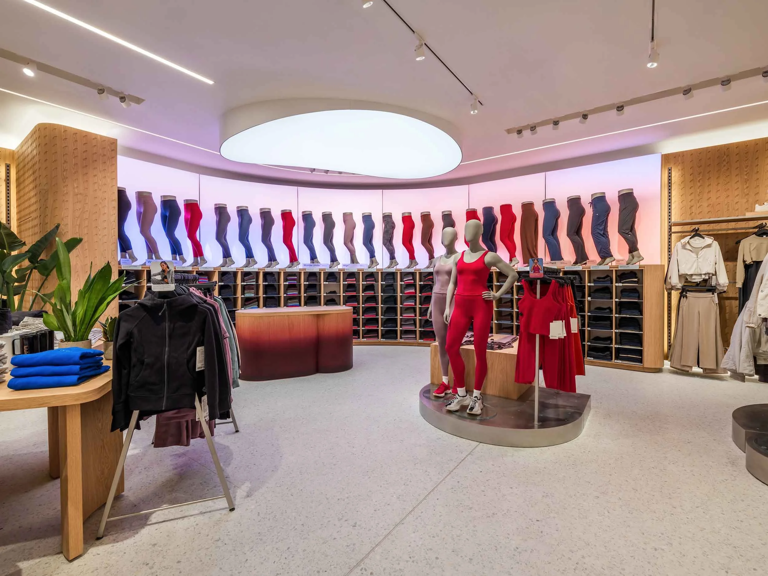 Mannequins dressed in red workout clothing, surrounded by shelves of folded clothes, in a retail store section for activewear.