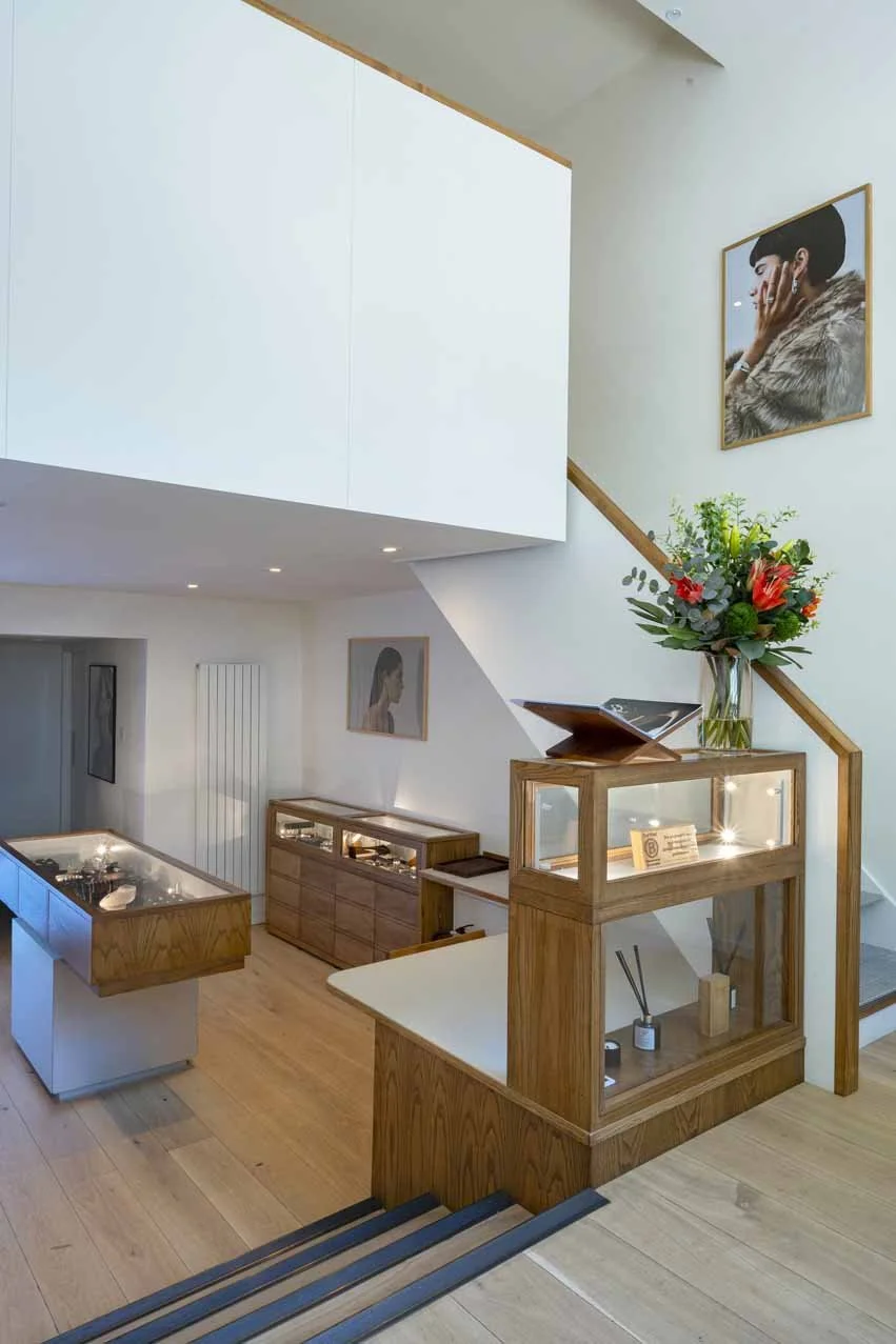 Interior of a modern, minimalist home with wooden stairs, a display case with decorative items, a large flower arrangement, and framed artwork on the walls.
