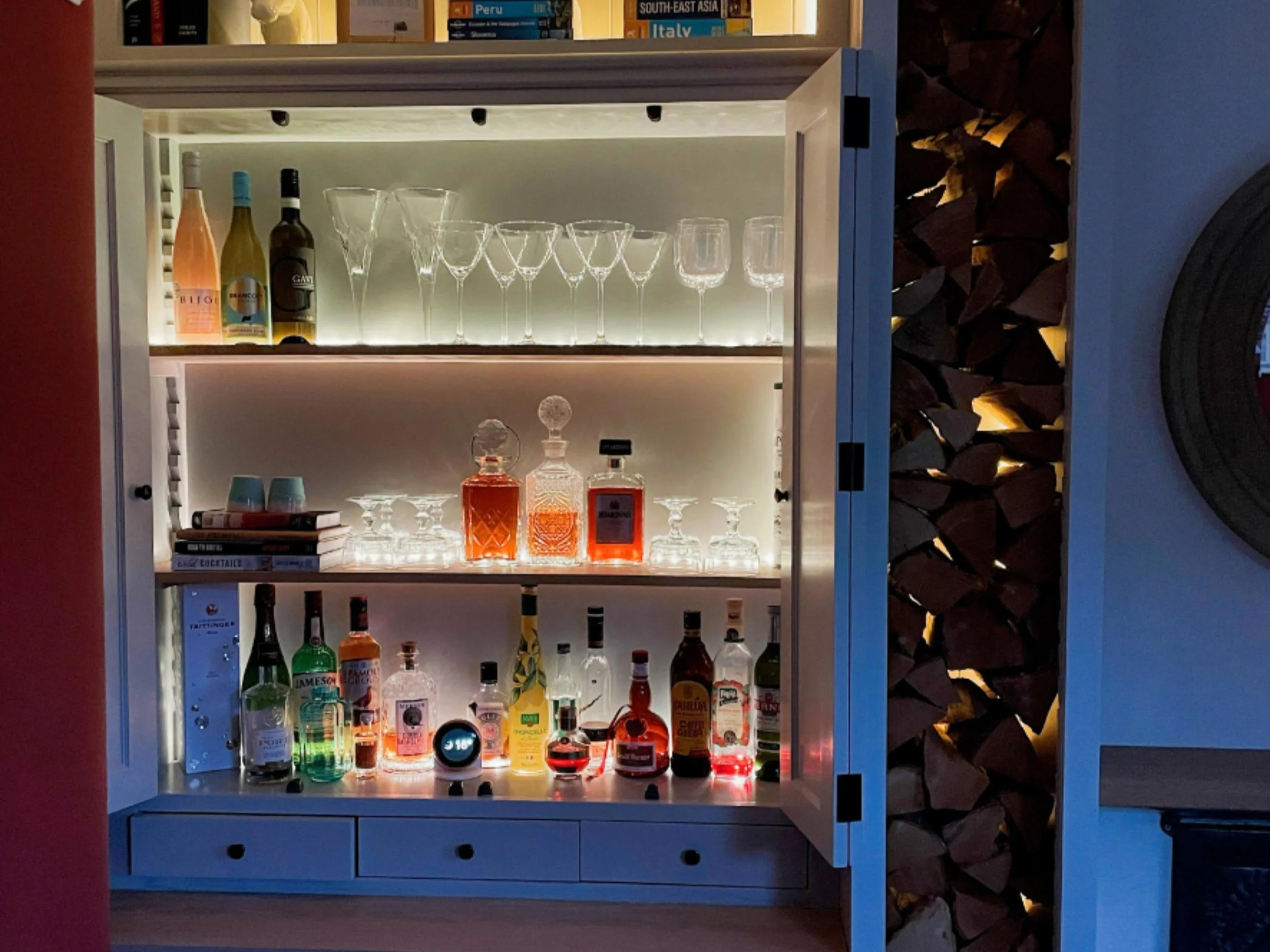 Bespoke illuminated drinks cabinet with glassware, decanters and neatly arranged spirits, designed with closeable doors so everything can be hidden from view.