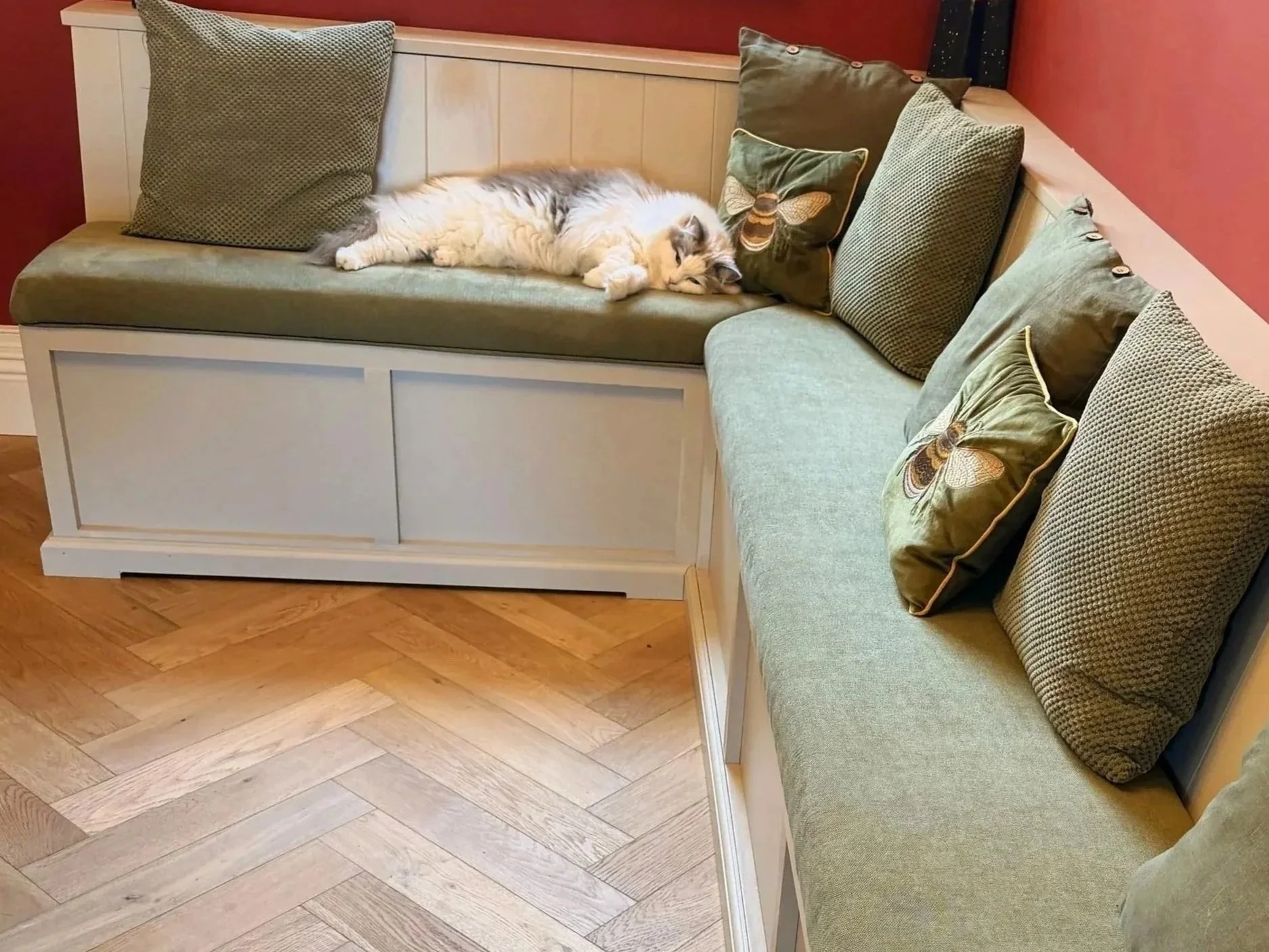 Bespoke built‑in corner bench with green cushions and decorative pillows, handcrafted to create a cosy, inviting seating nook in a warm, characterful room.