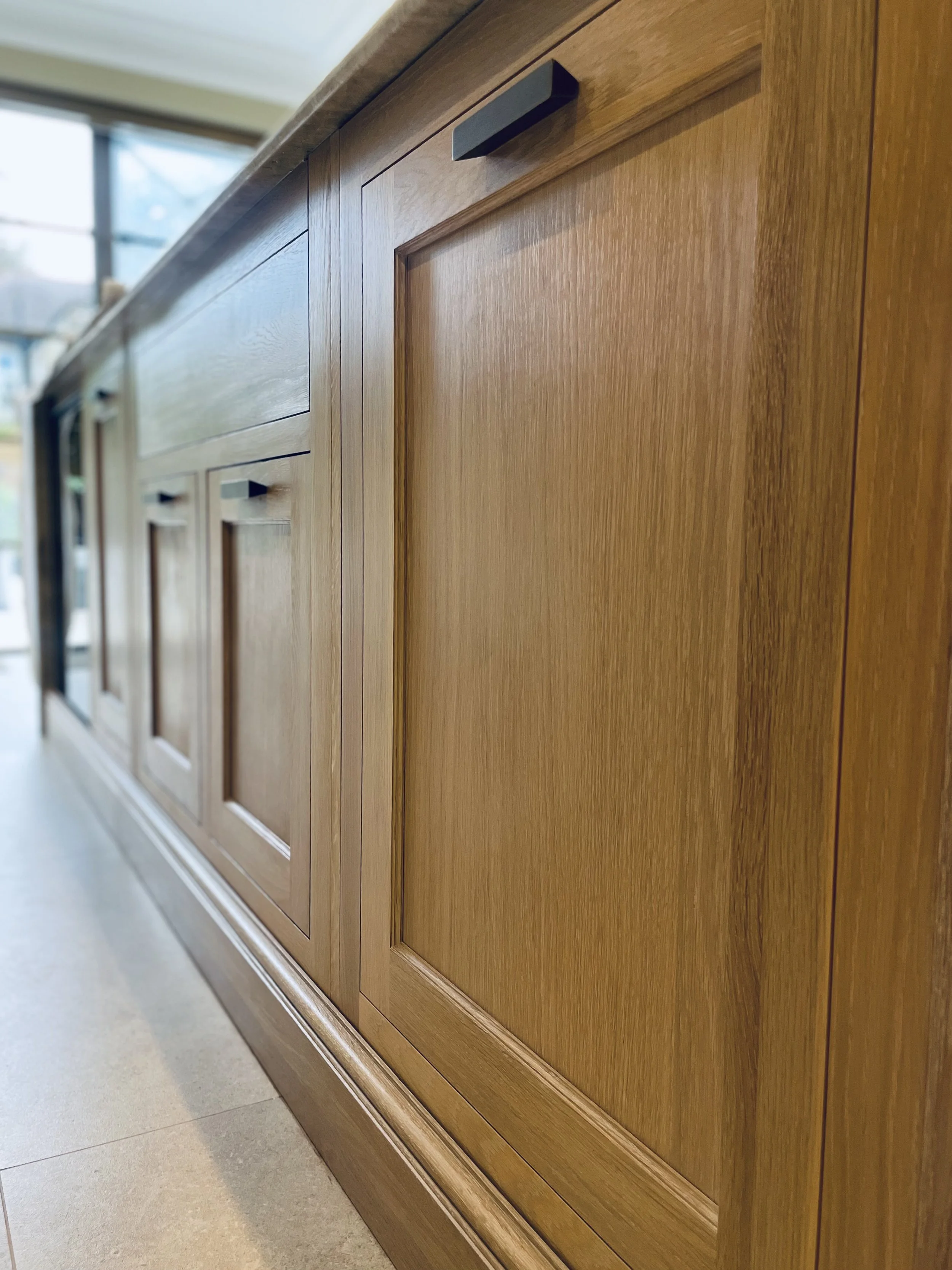 Bespoke oak kitchen cabinetry with recessed panel doors and black handles, showcasing the natural grain and handcrafted finish.