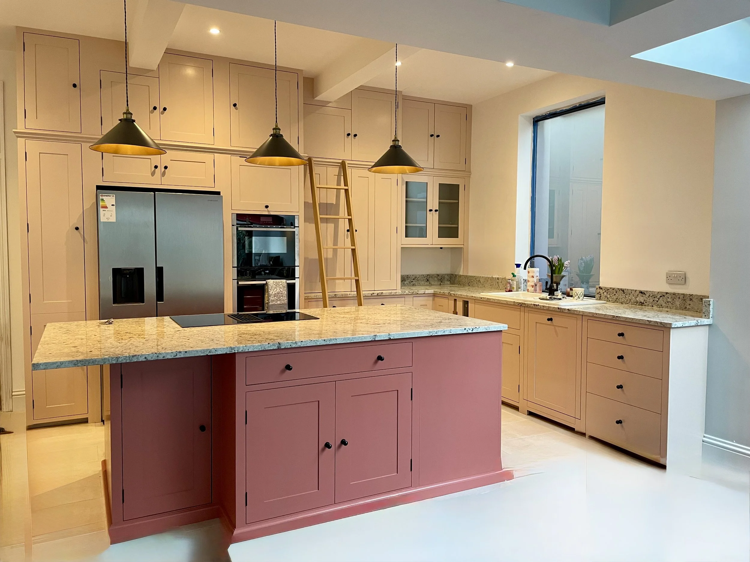 Bespoke handmade kitchen with pink island and tall fitted cabinetry, crafted with care by our family‑run workshop for a warm, functional cooking space.