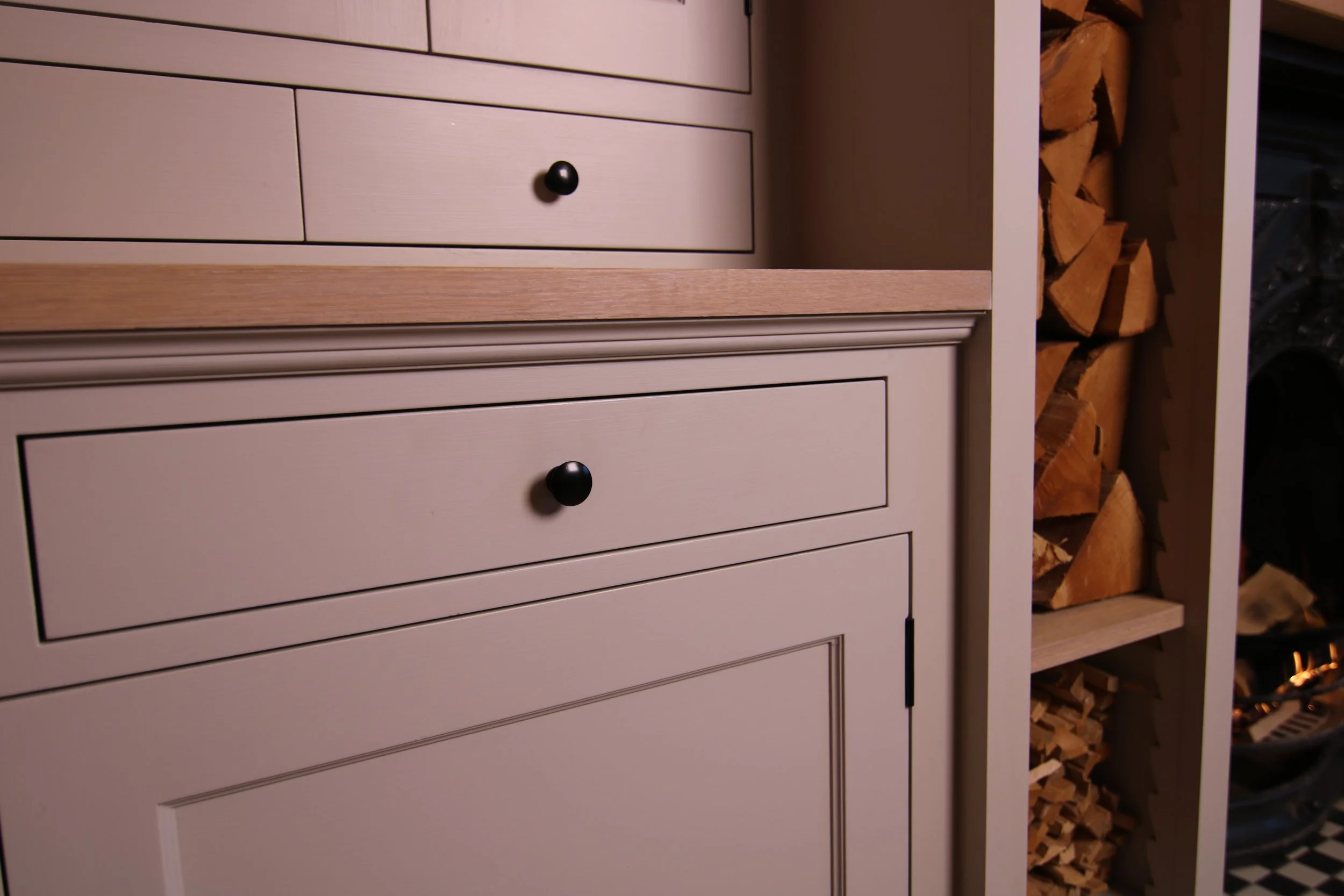 Close-up of beige cabinets with black knobs, next to a shelf filled with neatly stacked firewood.