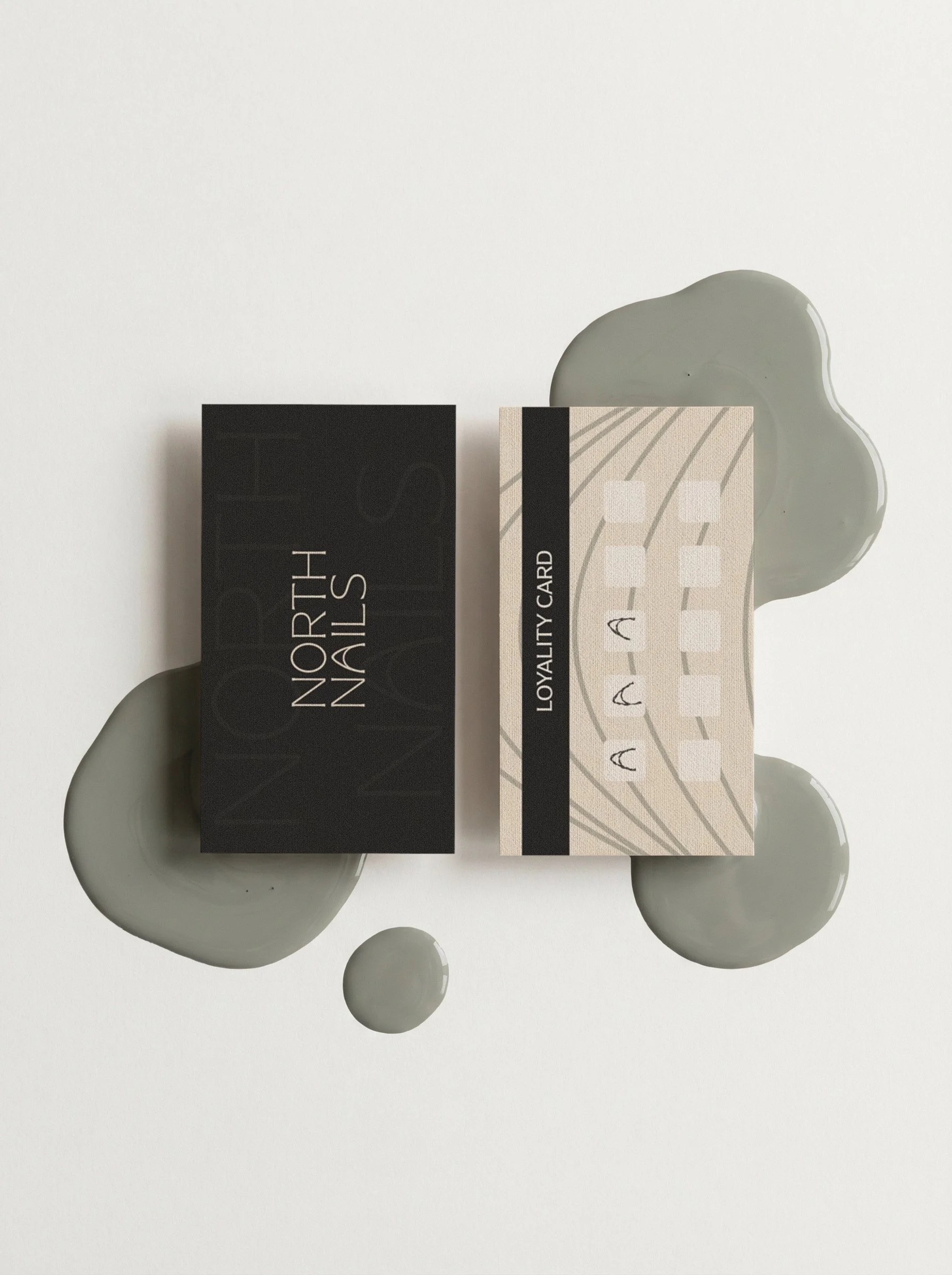 Two loyalty cards, one black and one beige with a barcode pattern, placed on a white surface with a gray paint smear around the cards.