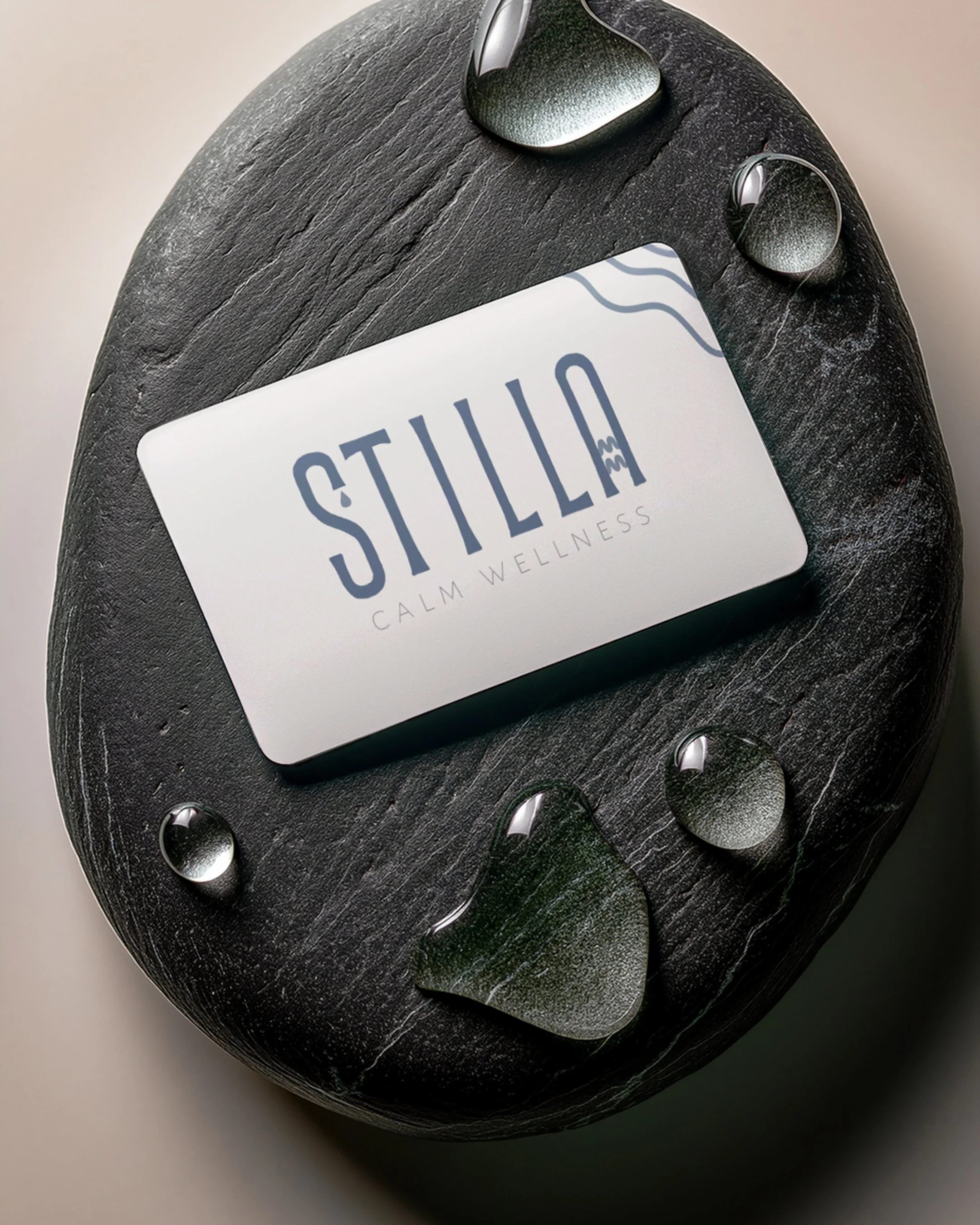 Close-up view of a black oval-shaped wellness device with water droplets on its surface, placed on a white surface. A white card with the word 'Stilla' is partially visible on the device.