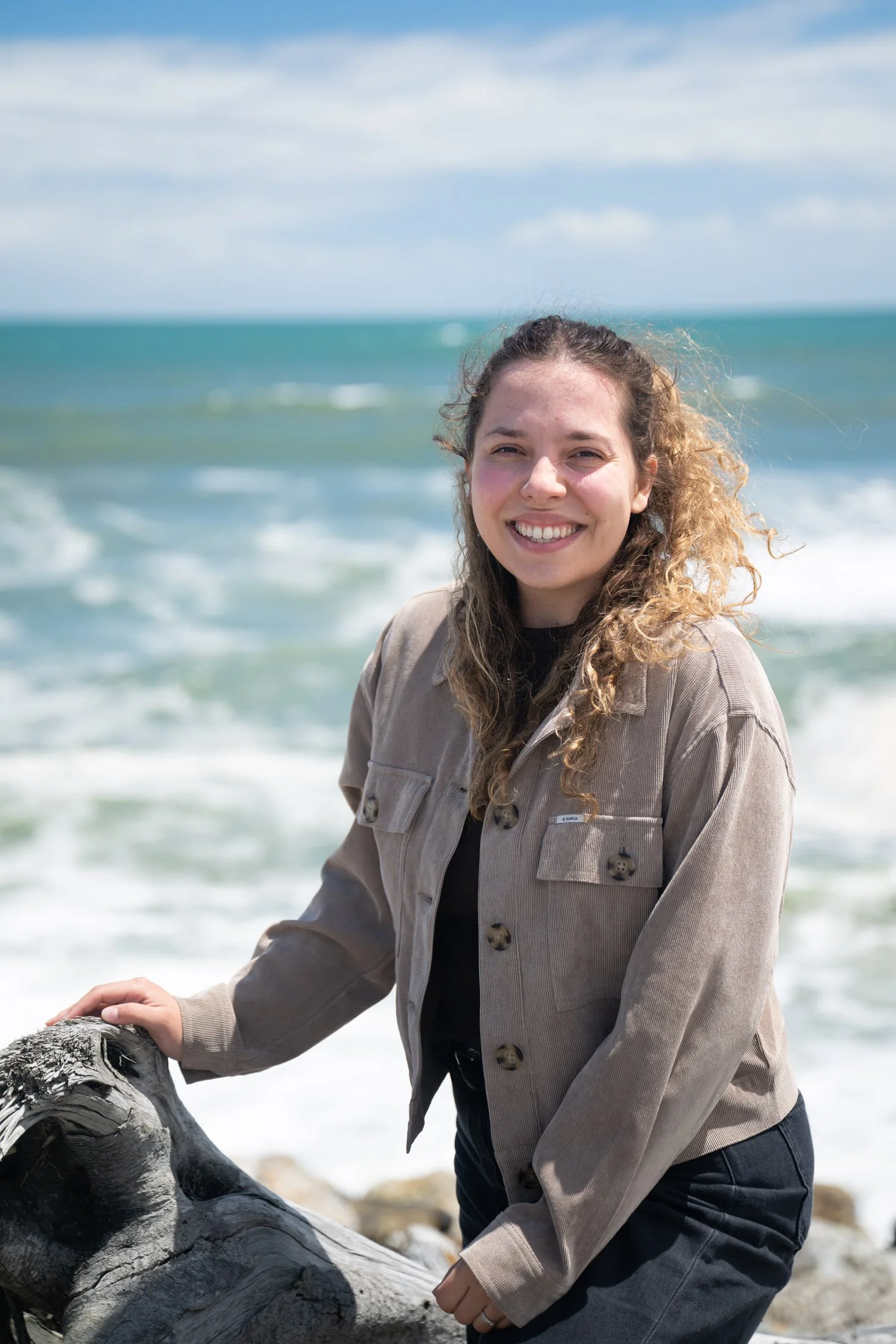 Junge Frau am Strand, lächelnd, mit Wasser und Himmel im Hintergrund. Dalia Schär.