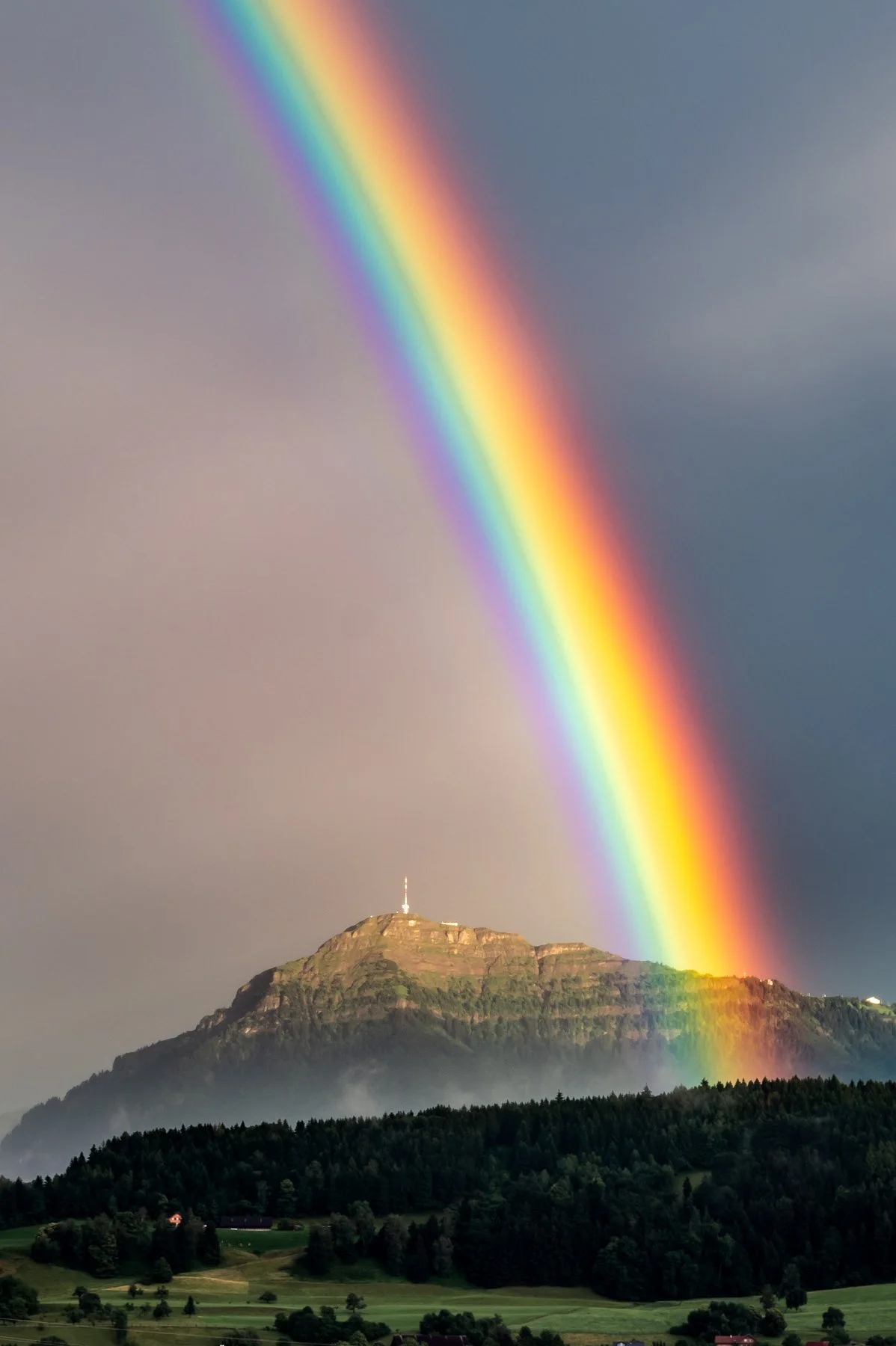 Regenbogen über dem Berg Rigi mit bewaldeter Basis am Tag.
