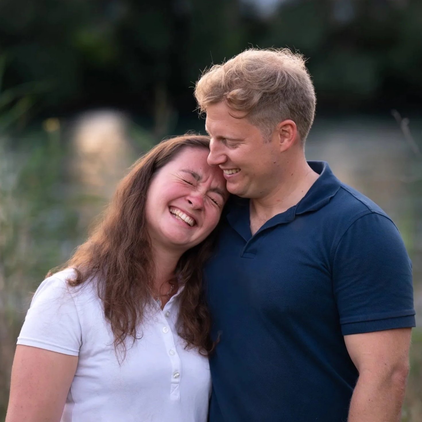 Ein lachendes Paar, das sich liebevoll berührt, draußen im Freien bei Sonnenuntergang.