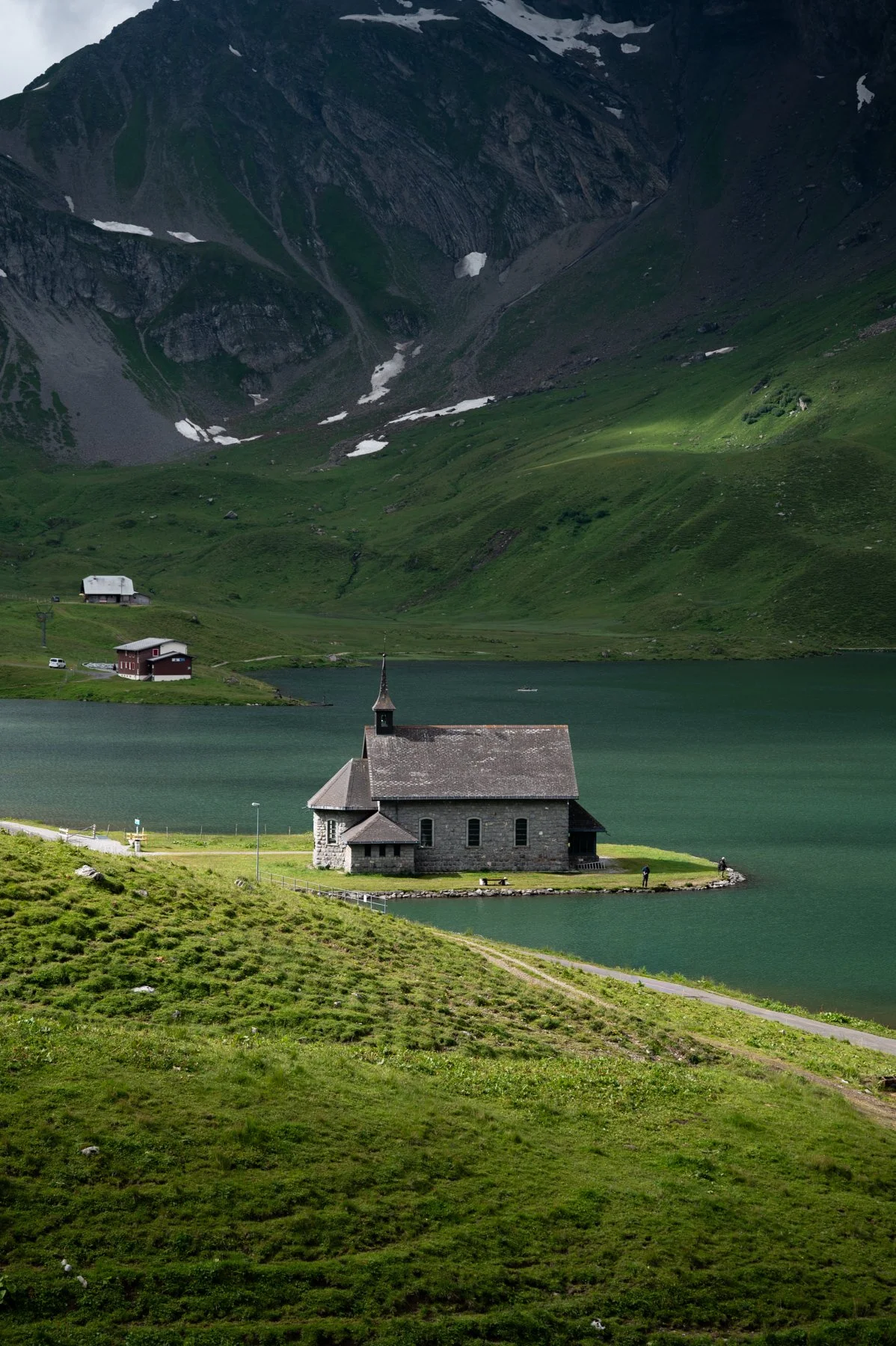 Eine kleine Kirche am Ufer eines Sees auf der Melchseefrutt, umgeben von grünen Hügeln und Bergen in einer ländlichen Region.