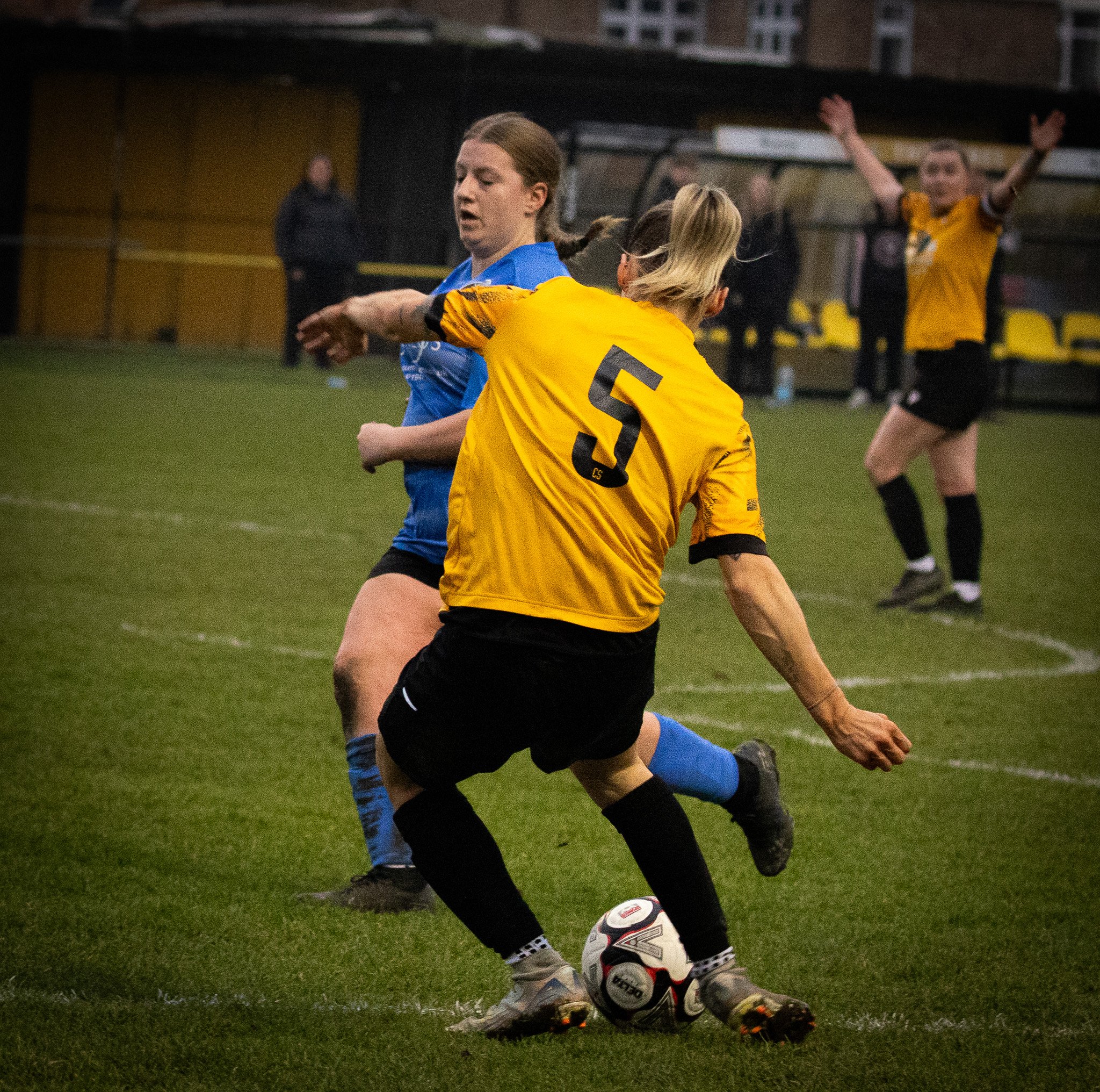 A women's soccer game with players in yellow and blue jerseys actively competing on the field at night.