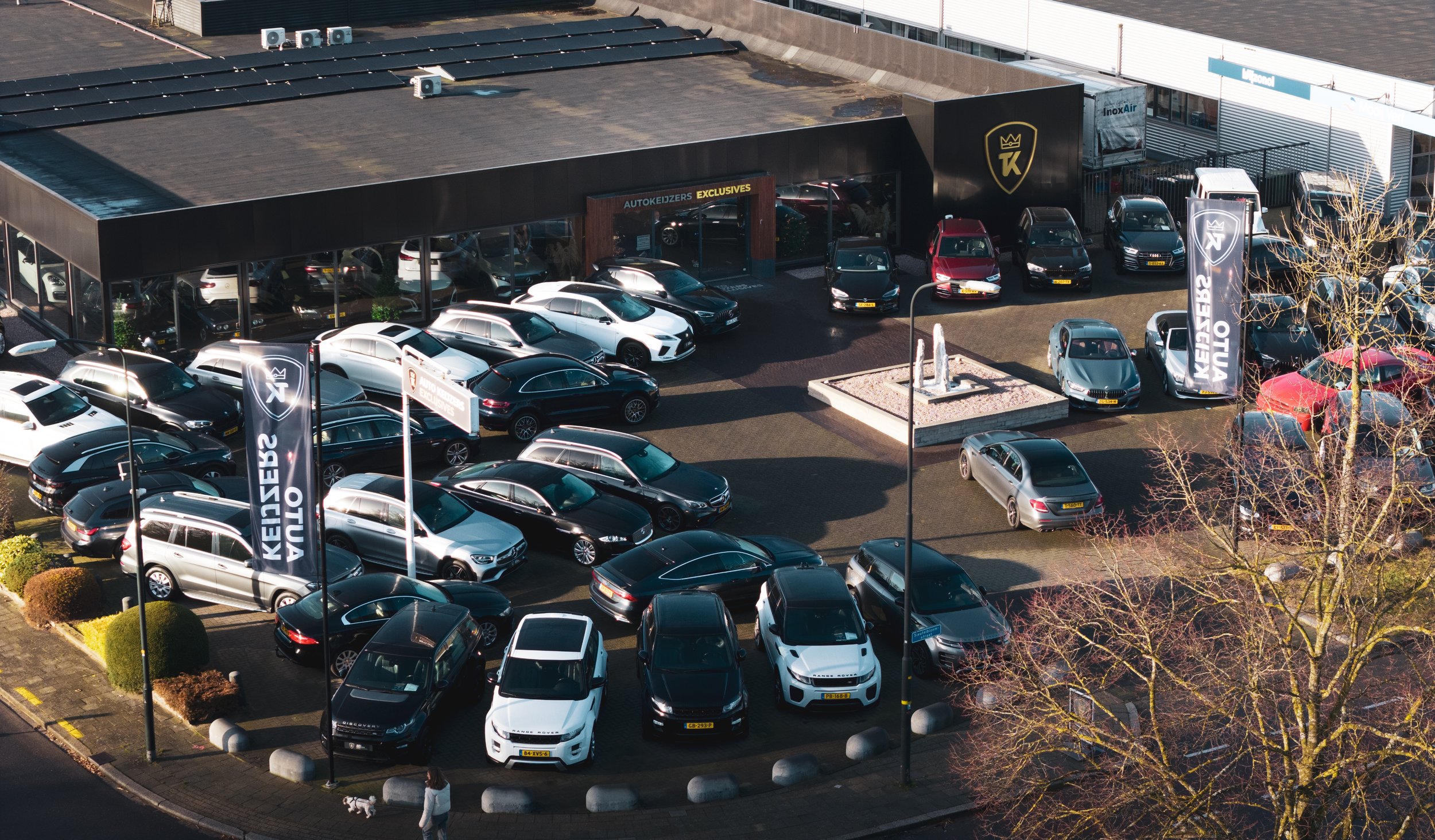 Een autodealer met parkeergarage vol verschillende auto's, vlaggen en promotieborden buiten.