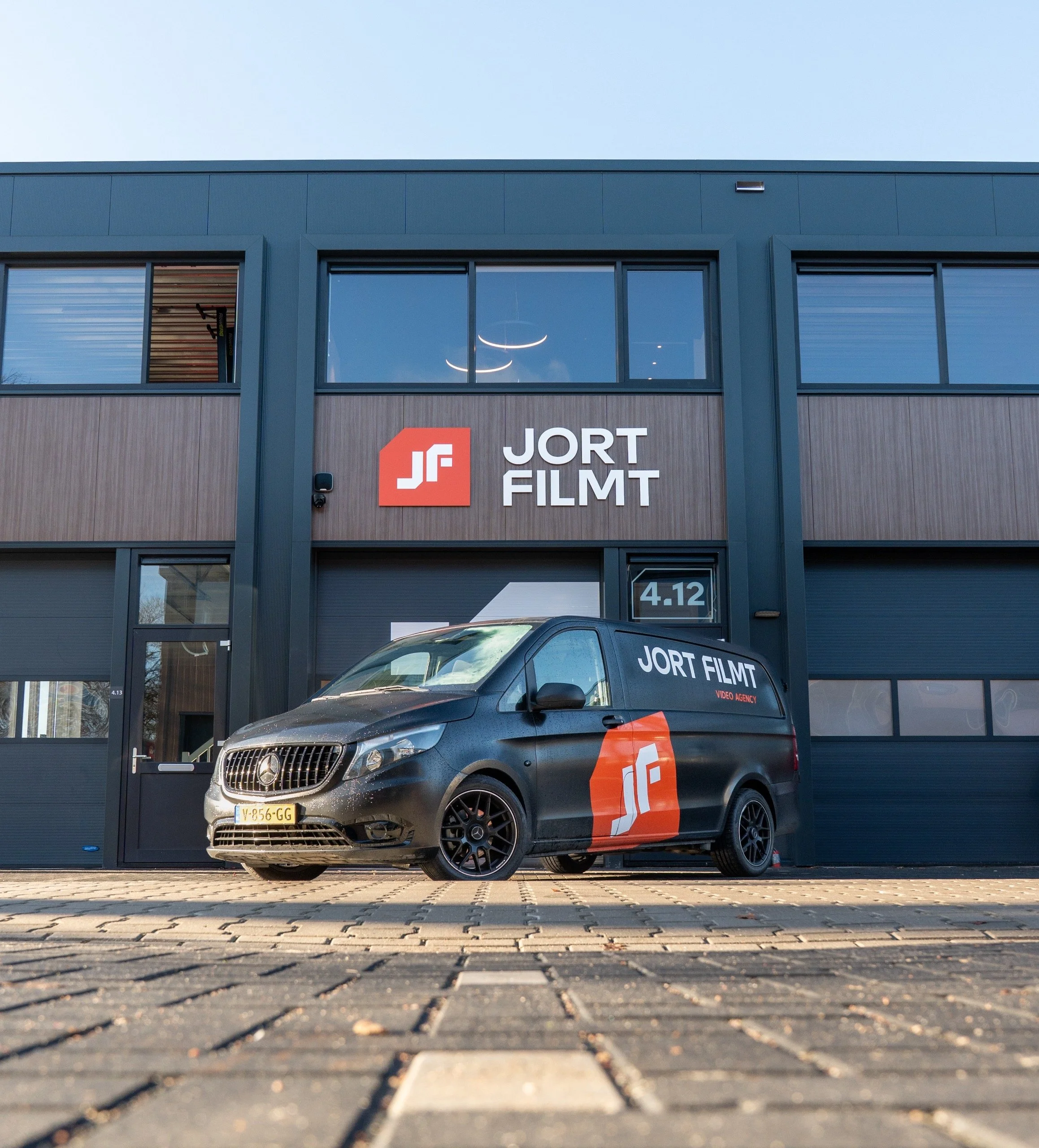 Een bedrijfsgebouw met het logo 'JORT FILMT' en een zwarte bedrijfsauto voor de ingang, beide met het logo en naam 'JORT FILMT'.
