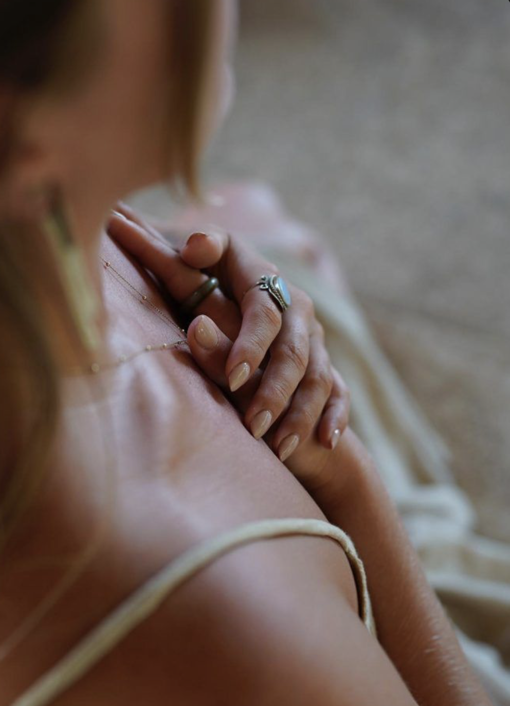 A close-up of a woman with well-manicured nails wearing rings, holding her hand over her chest.