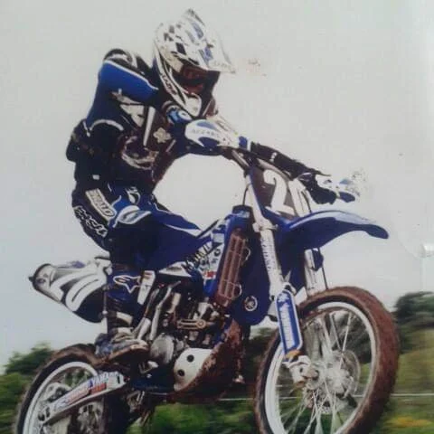 Motocross rider wearing a helmet and gear riding a dirt bike on a trail.