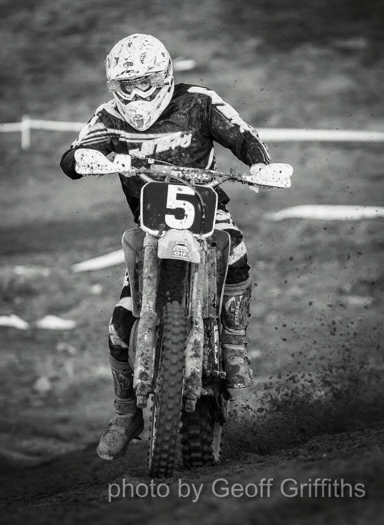 A motocross rider in protective gear, riding a dirt bike with the number 5 on the front, on a muddy track.