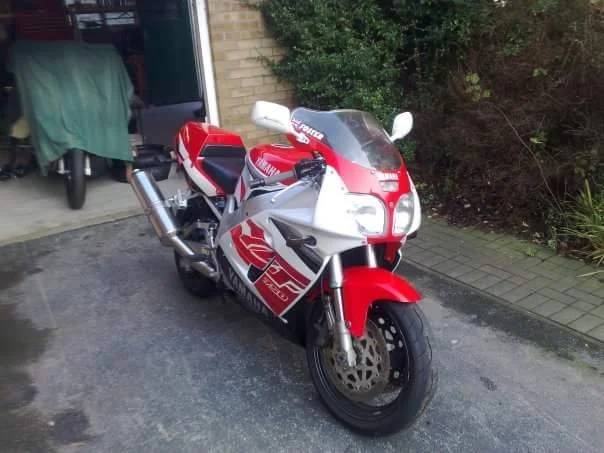 Red and white Honda CBR motorcycle parked outside a house, next to a garage with a cover and some items inside.