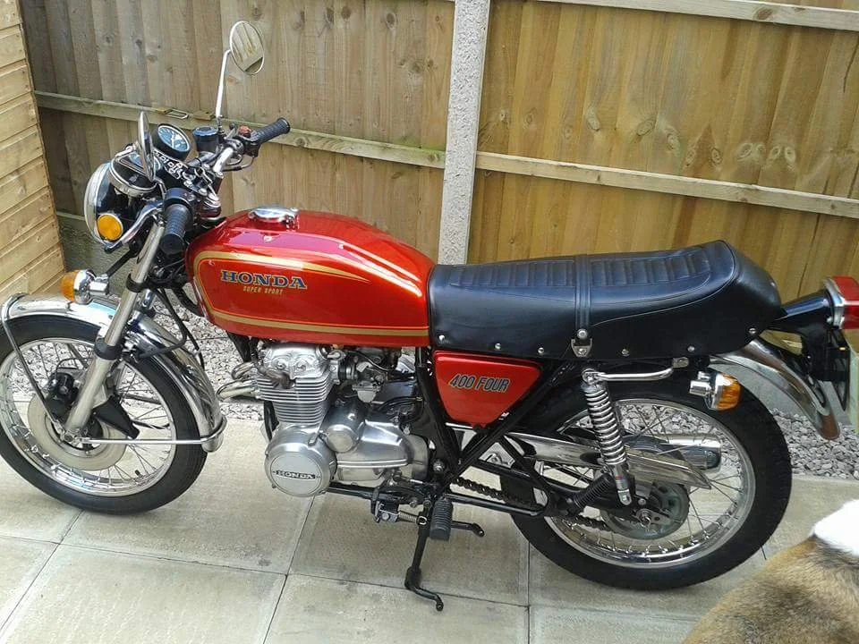 Red Honda Super Sport motorcycle parked on a concrete surface with a wooden fence in the background.