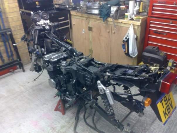 Disassembled motorcycle in a workshop with tools and equipment in the background.