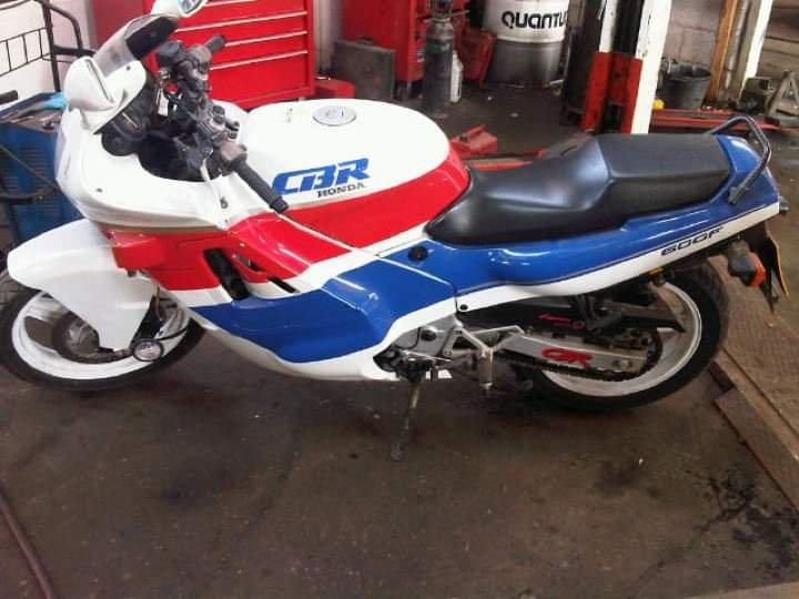 A vintage Honda motorcycle in a garage, painted with red, white, and blue colors, featuring the model number '600F' on the side and 'CBR' branding on the fuel tank.