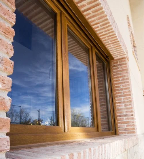Fenêtre en bois avec vitre reflective sur un mur en briques rouges, reflet du ciel bleu avec nuages.