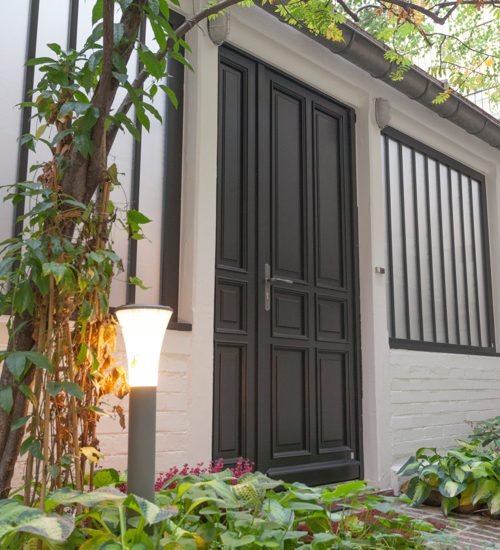 Portail noir avec double porte, entouré de végétation verte et éclairage extérieur