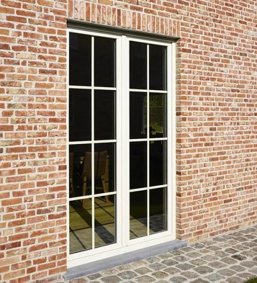 Fenêtre en verre avec cadre blanc, installée dans un mur en briques rouges, donnant sur une salle avec une table et des chaises.