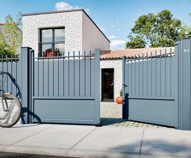 Vue d'une maison moderne avec une porte de clôture bleue, un vélo à gauche, et un arbre en arrière-plan.