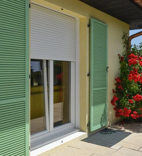Fenêtre avec volet vert et volets verts à côtés, côté extérieur d'une maison avec fleurs rouges