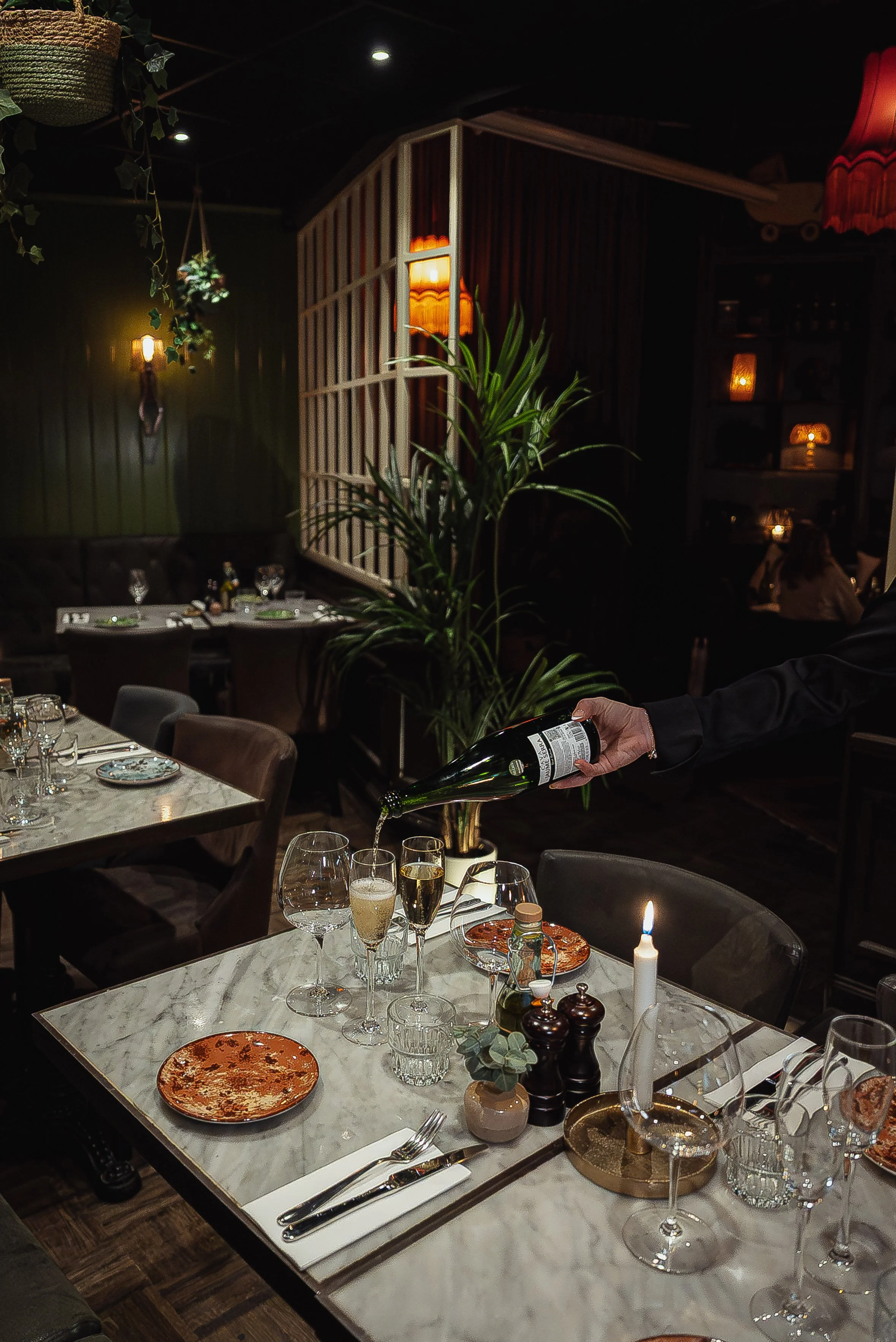 Person som serverar champagne på ett elegant middagsbord i en restaurang med dämpad belysning.