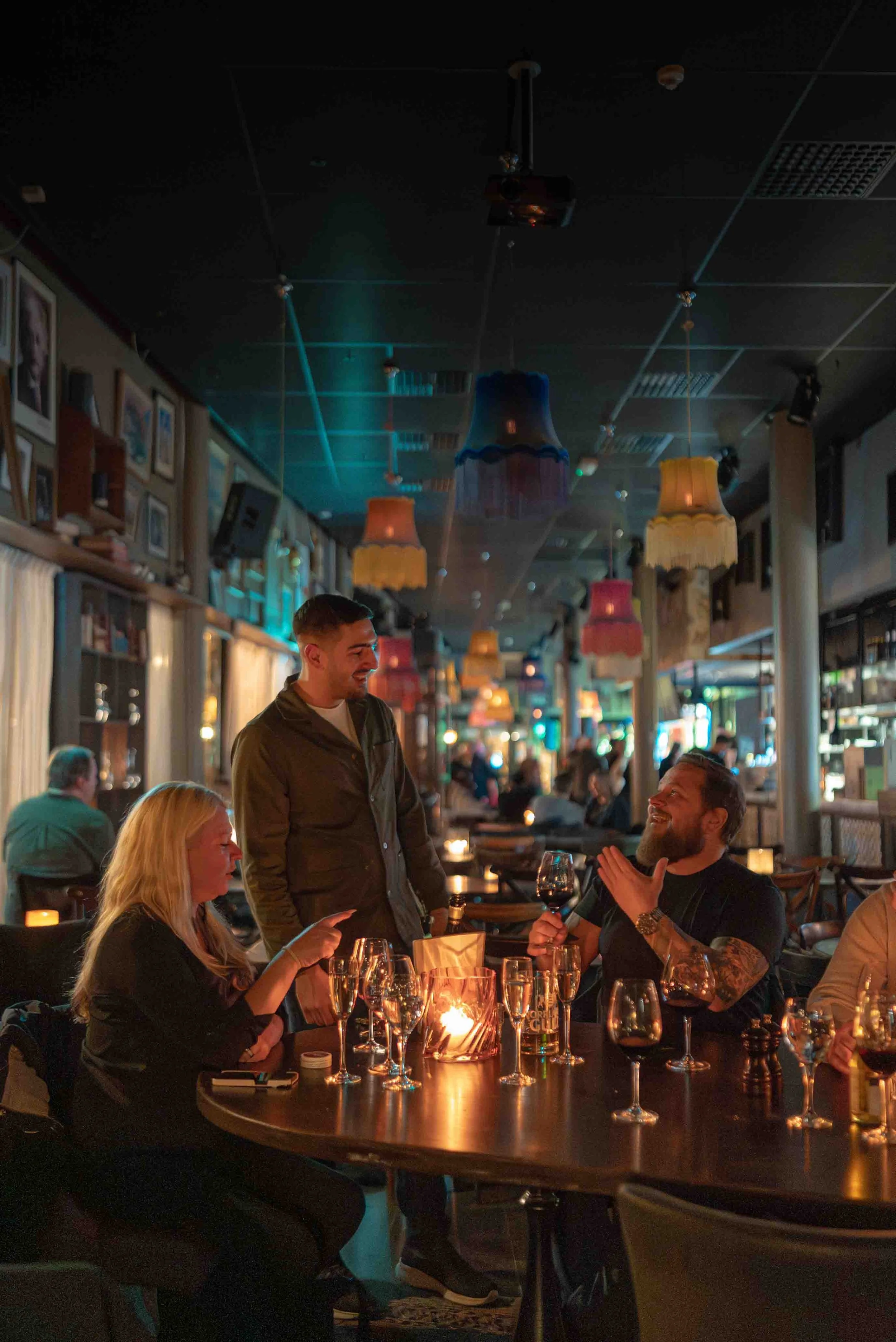 Människor som pratar och skrattar i ett mysigt restaurang- eller bar-miljö med vin på bordet och dimmad belysning.