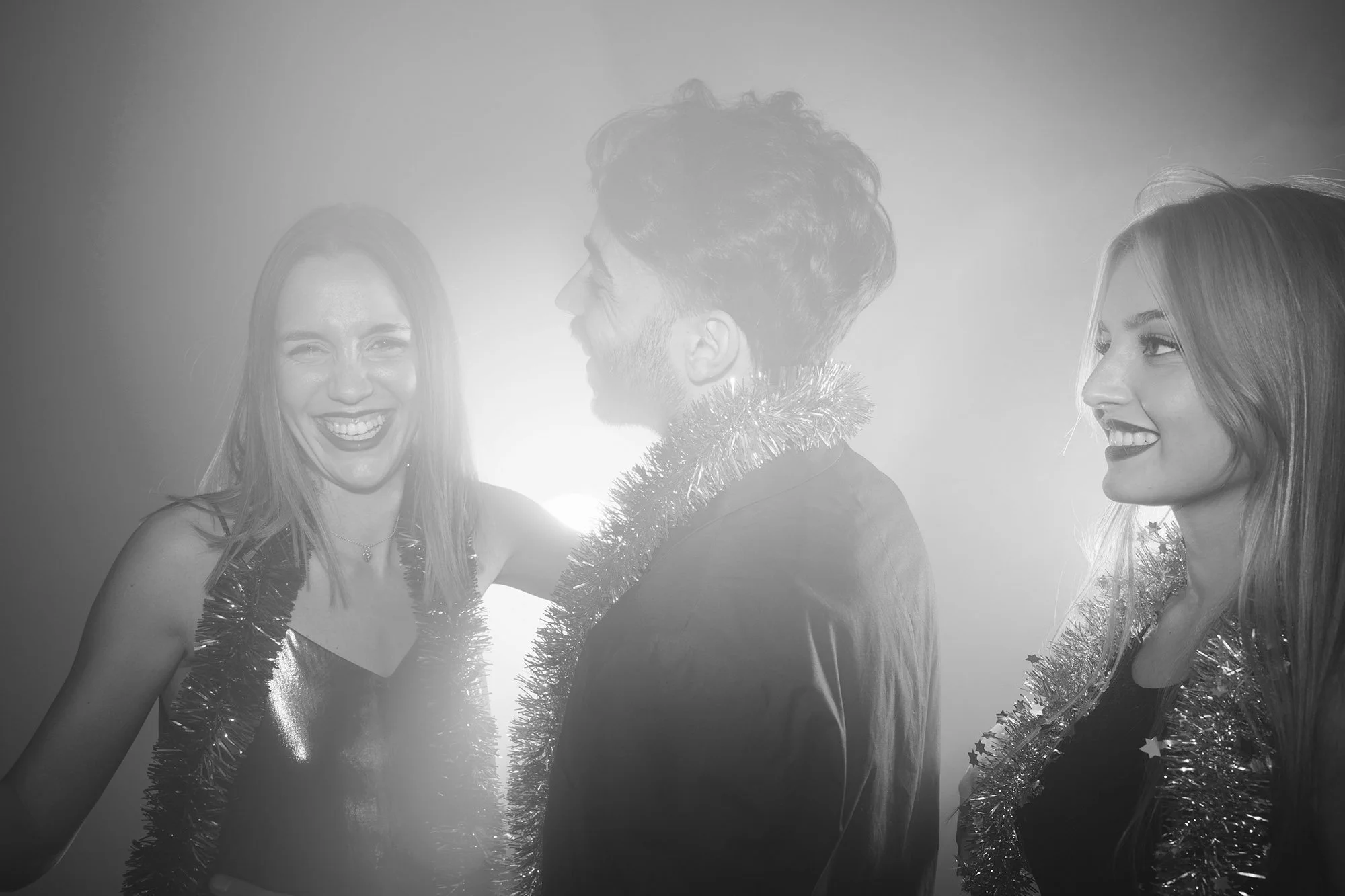 Tre unga personer firar med julgransglitter och leenden, två kvinnor och en man, i en festlig atmosfär