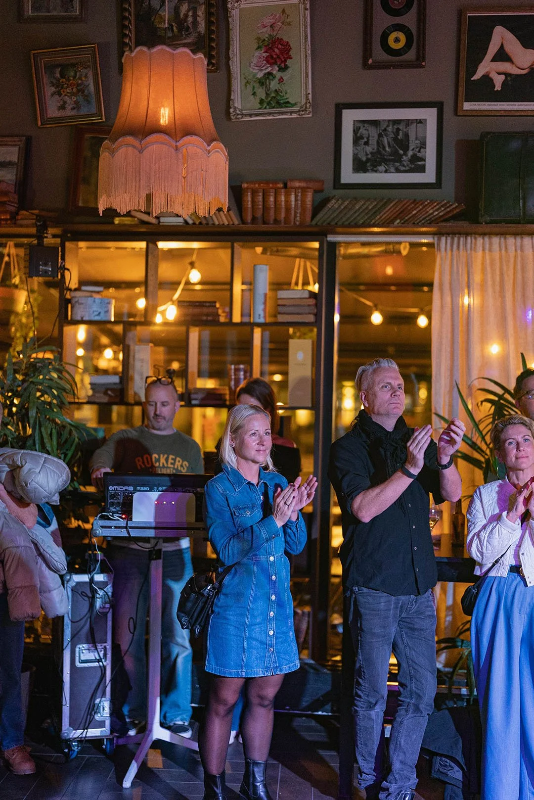 En grupp människor som står och tittar på en presentation eller scen i ett café eller restaurant med väggdekorationer och varma belysning.