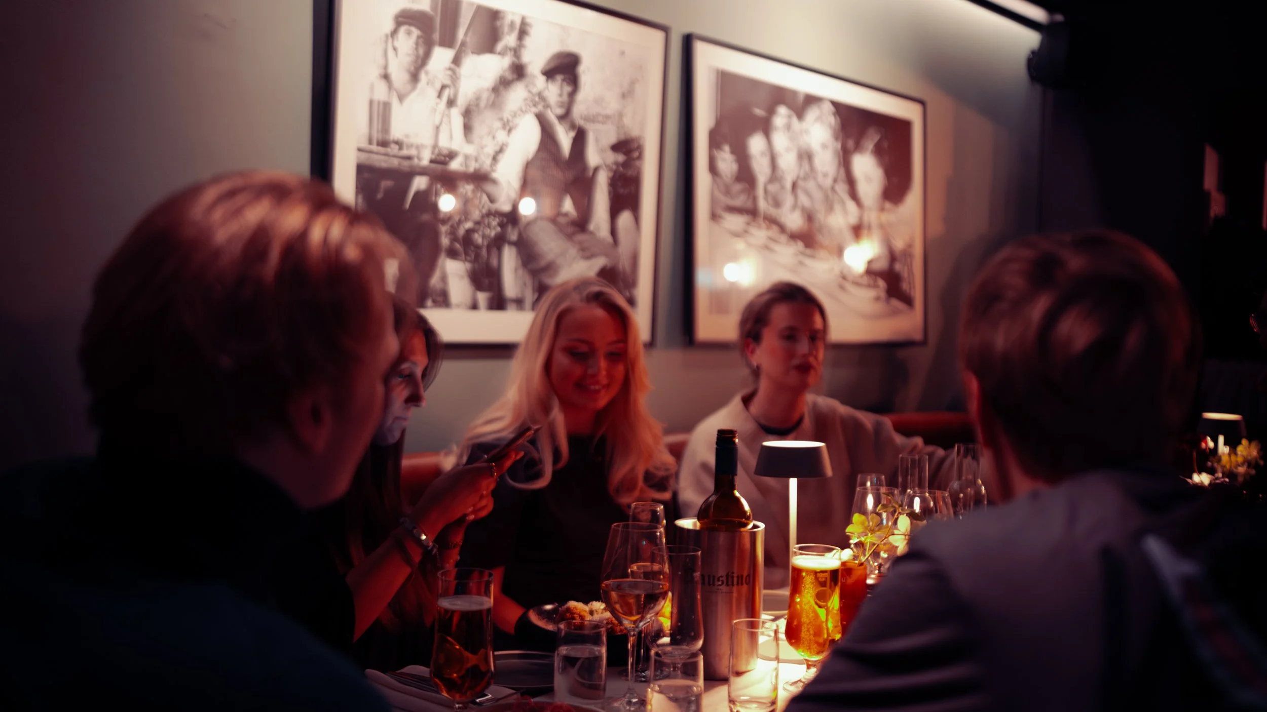 Group of five people enjoying dinner in a dimly lit restaurant with framed artwork on the wall behind them.