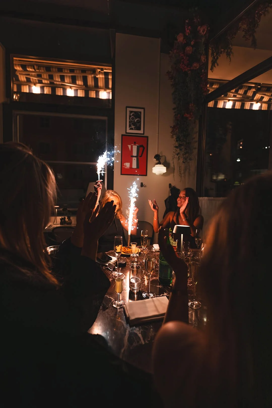 People celebrating at a dinner party with sparklers and champagne in a dimly lit restaurant or bar.
