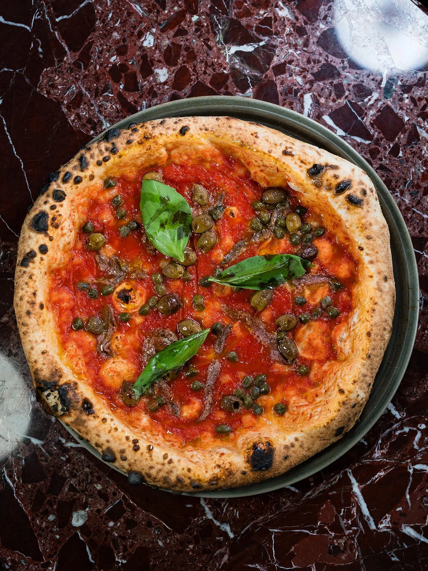Pizza med tomatsås, gröna basilablad och svarta oliver på en marmor bord.