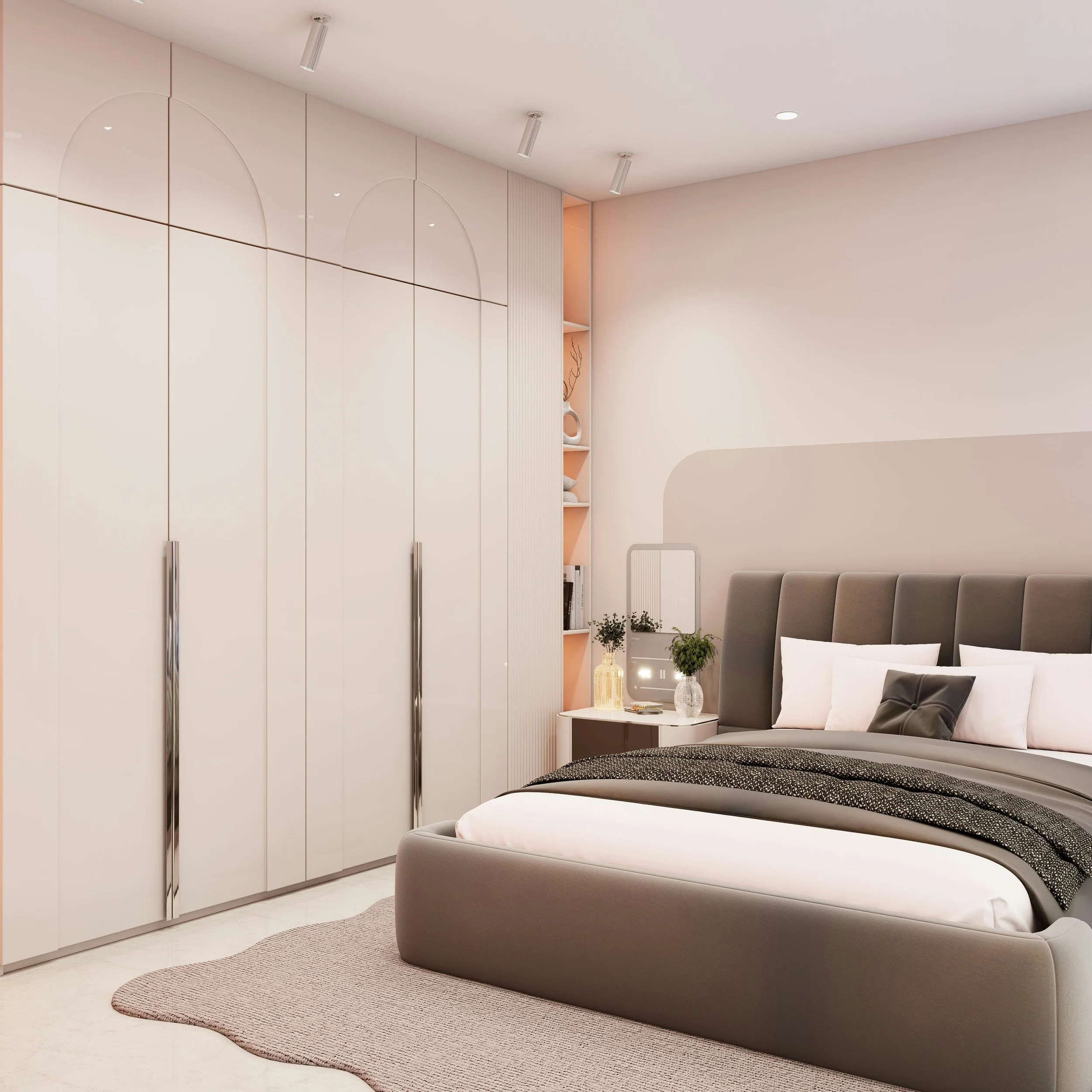 Modern bedroom with a large bed featuring a gray upholstered headboard, white and gray bedding, and decorative pillows. A bedside table with plants, decorative items, and a mirror is visible, alongside built-in closets and open shelving with decorative objects. The room has soft lighting and minimalist decor.