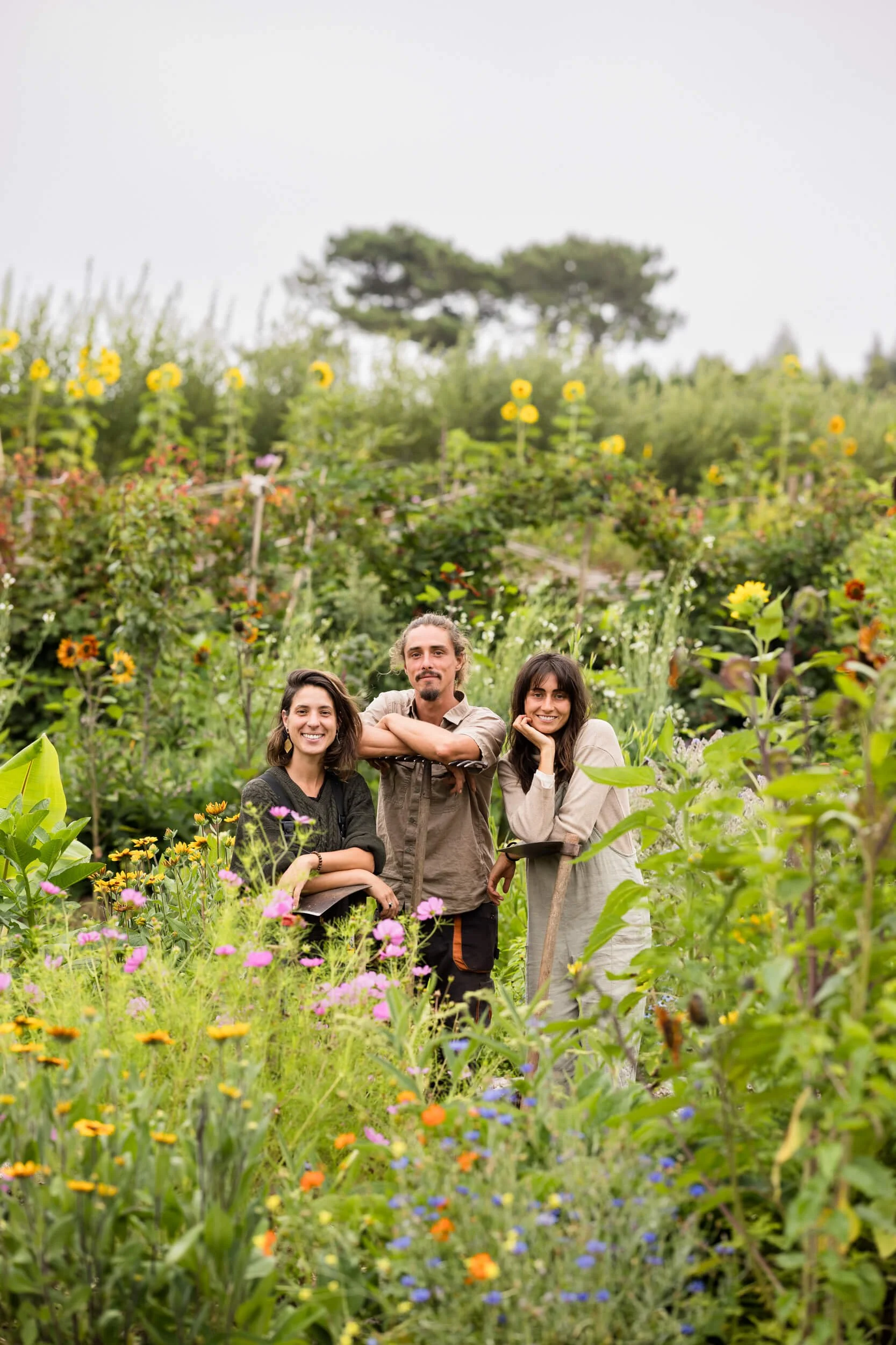 Three people in a lush garden with colorful flowers and sunflowers.