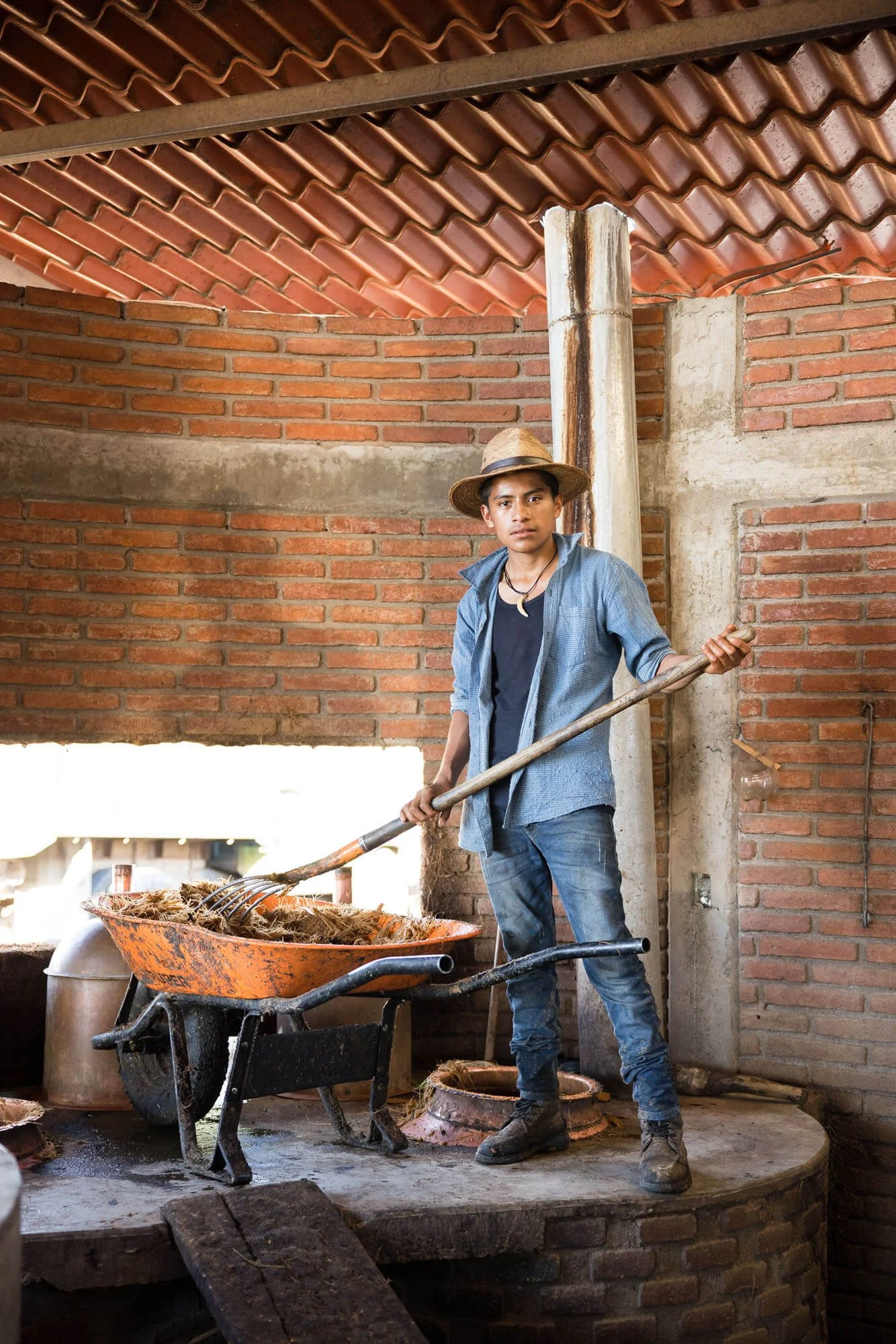 Man in straw hat working with a wheelbarrow in a brick room