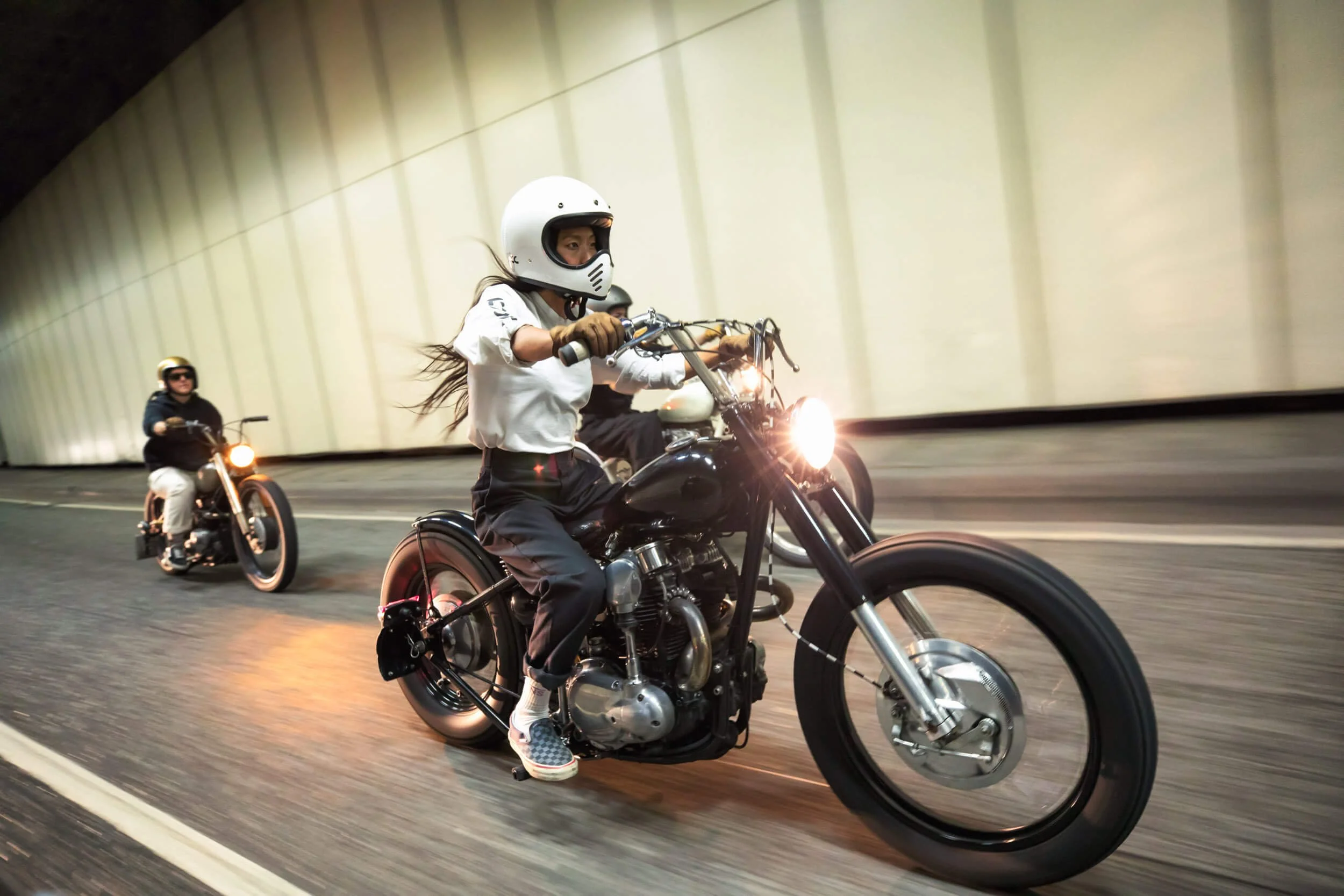 Two people riding motorcycles in a tunnel, with one wearing a white helmet and the other a black helmet.
