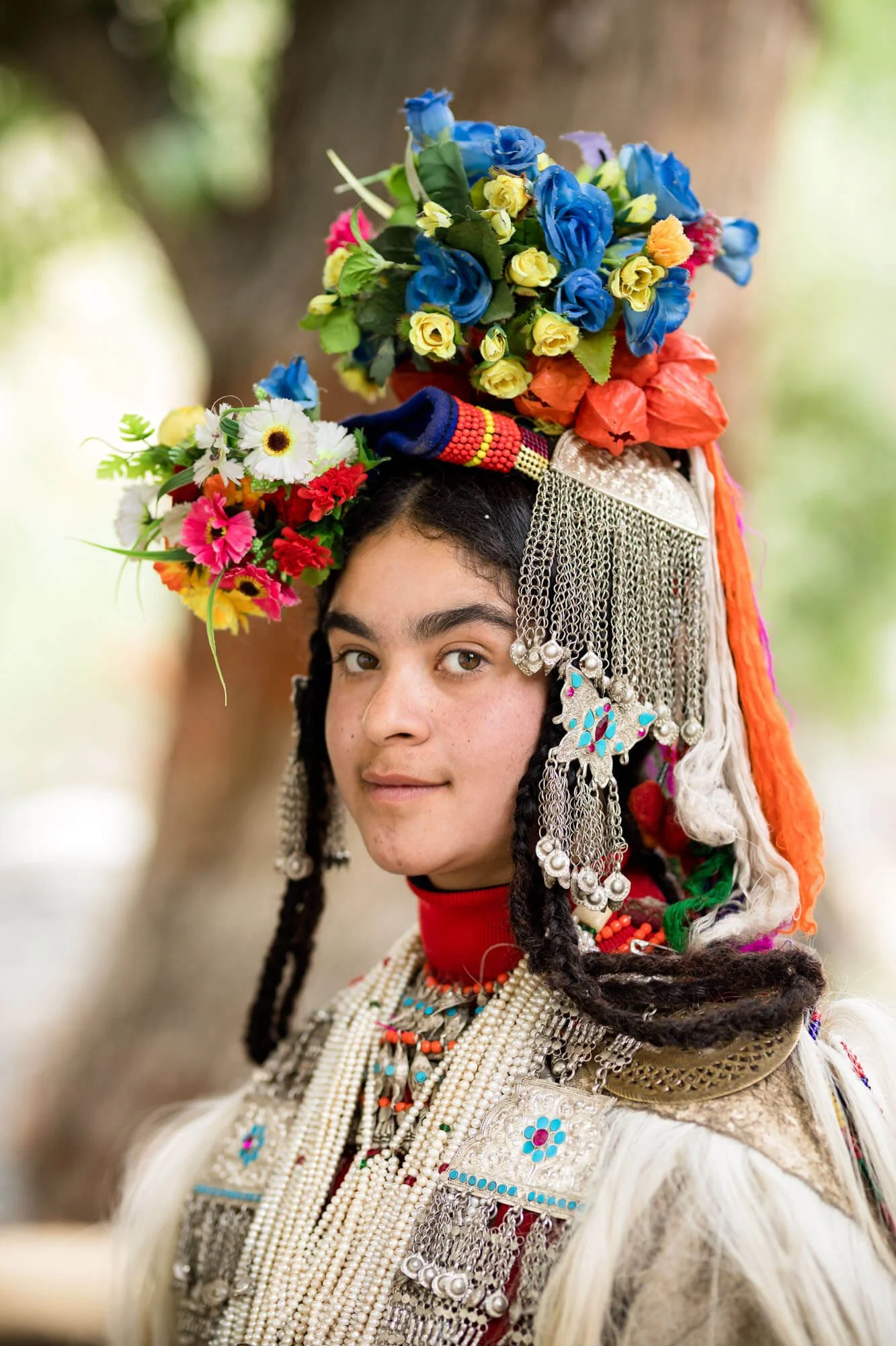 Person wearing traditional attire with colorful flowers, beads, and intricate jewelry on head.