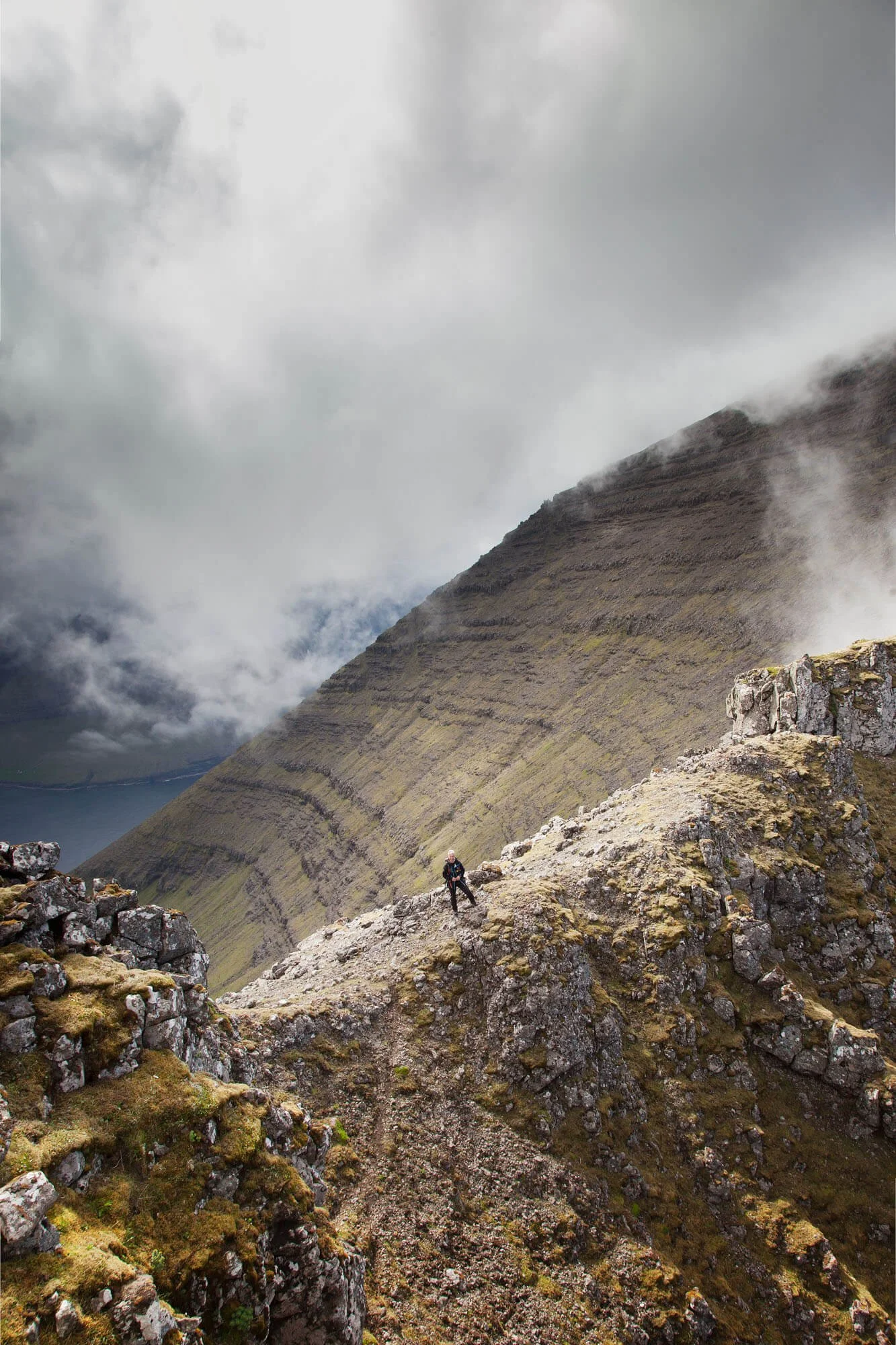 Hiker standing on a rocky mountain ridge with clouds and rugged terrain.