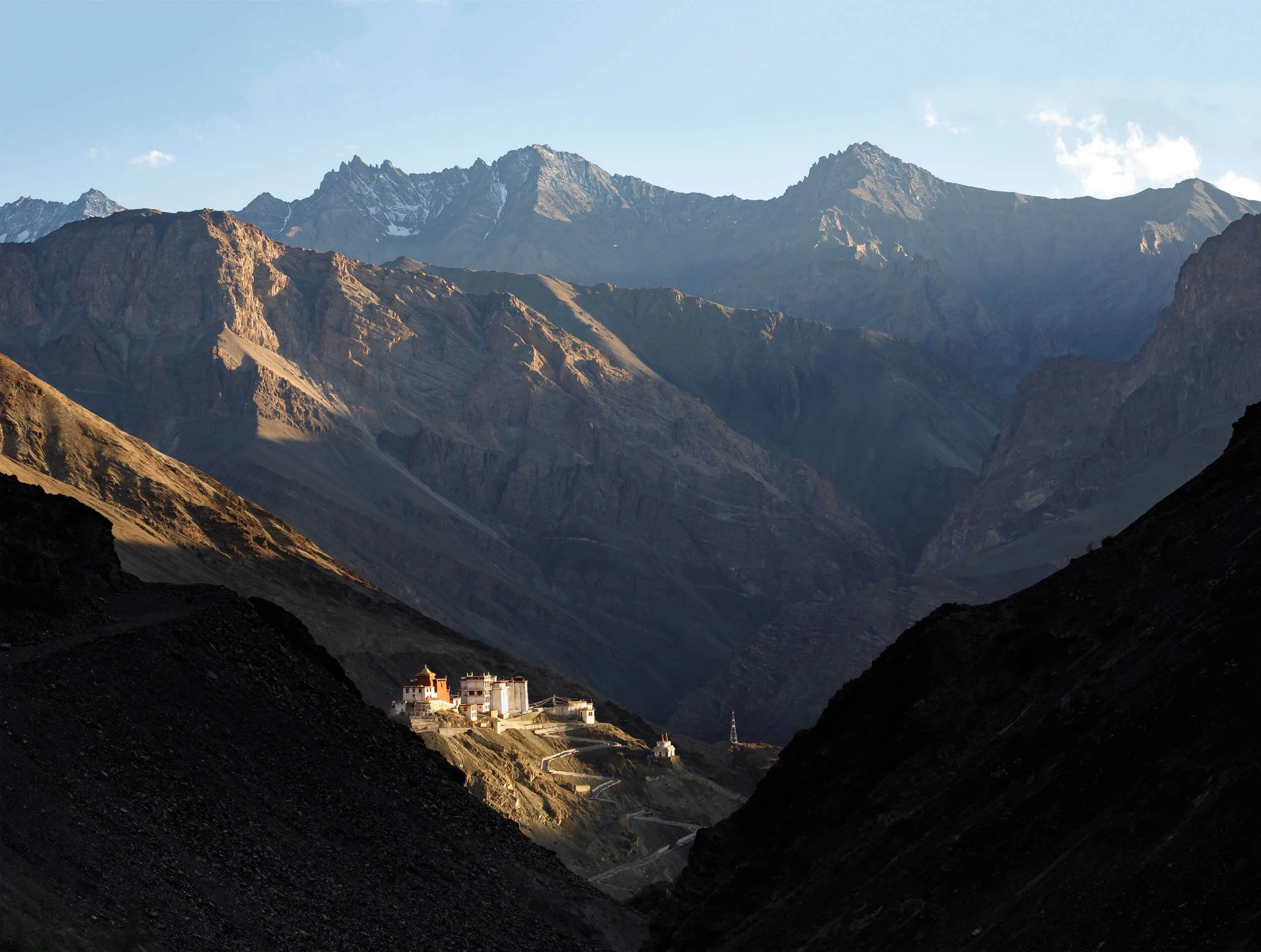 A remote Buddhist monastery situated in a mountainous valley at sunrise, with rugged peaks in the background.