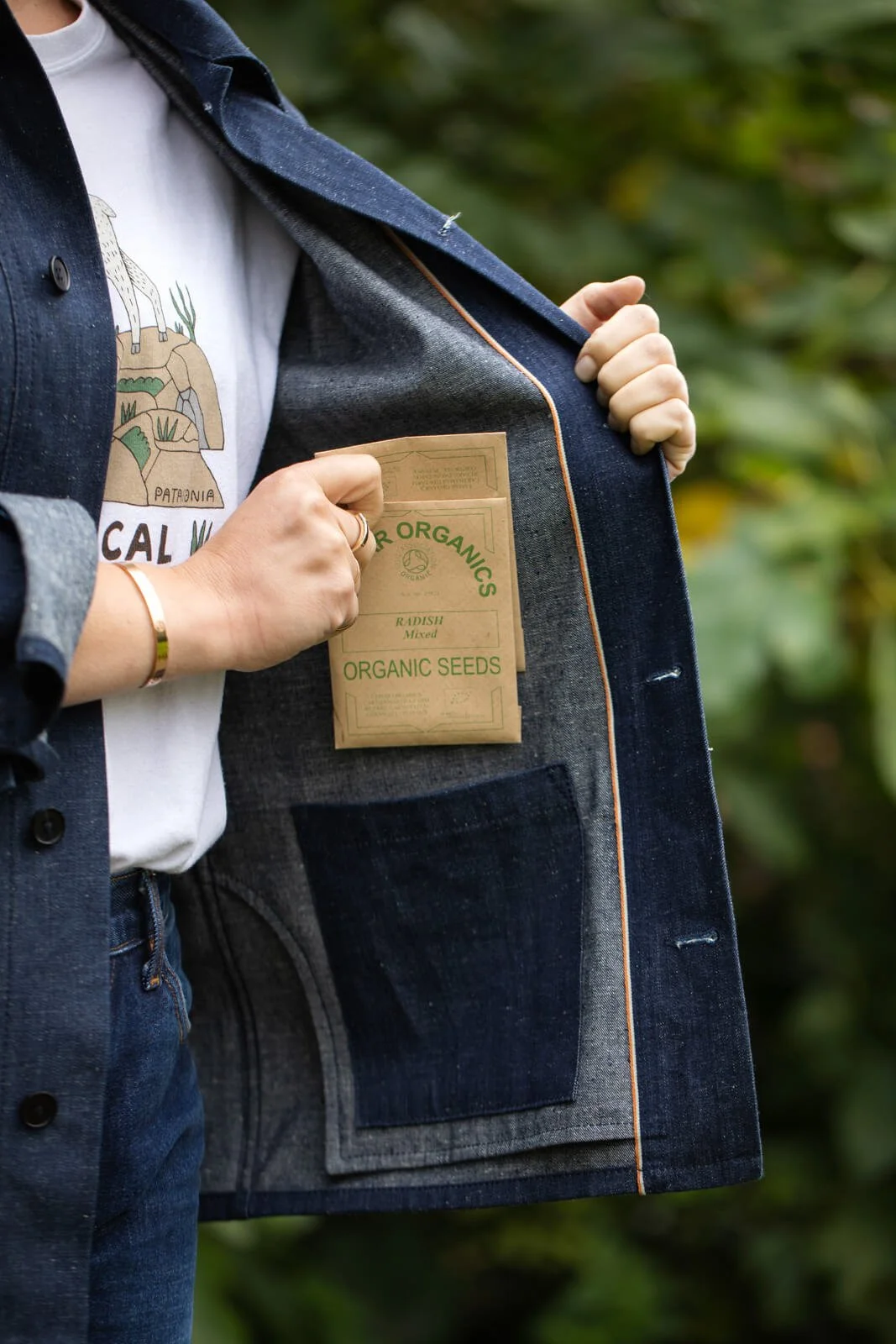 Hands Placing Organic Seed Packet Inside Denim Garden Jacket Pocket