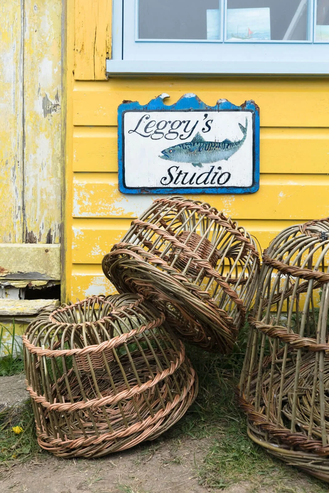 Wicker baskets stacked outside Leggy's Studio with a yellow wooden wall background.