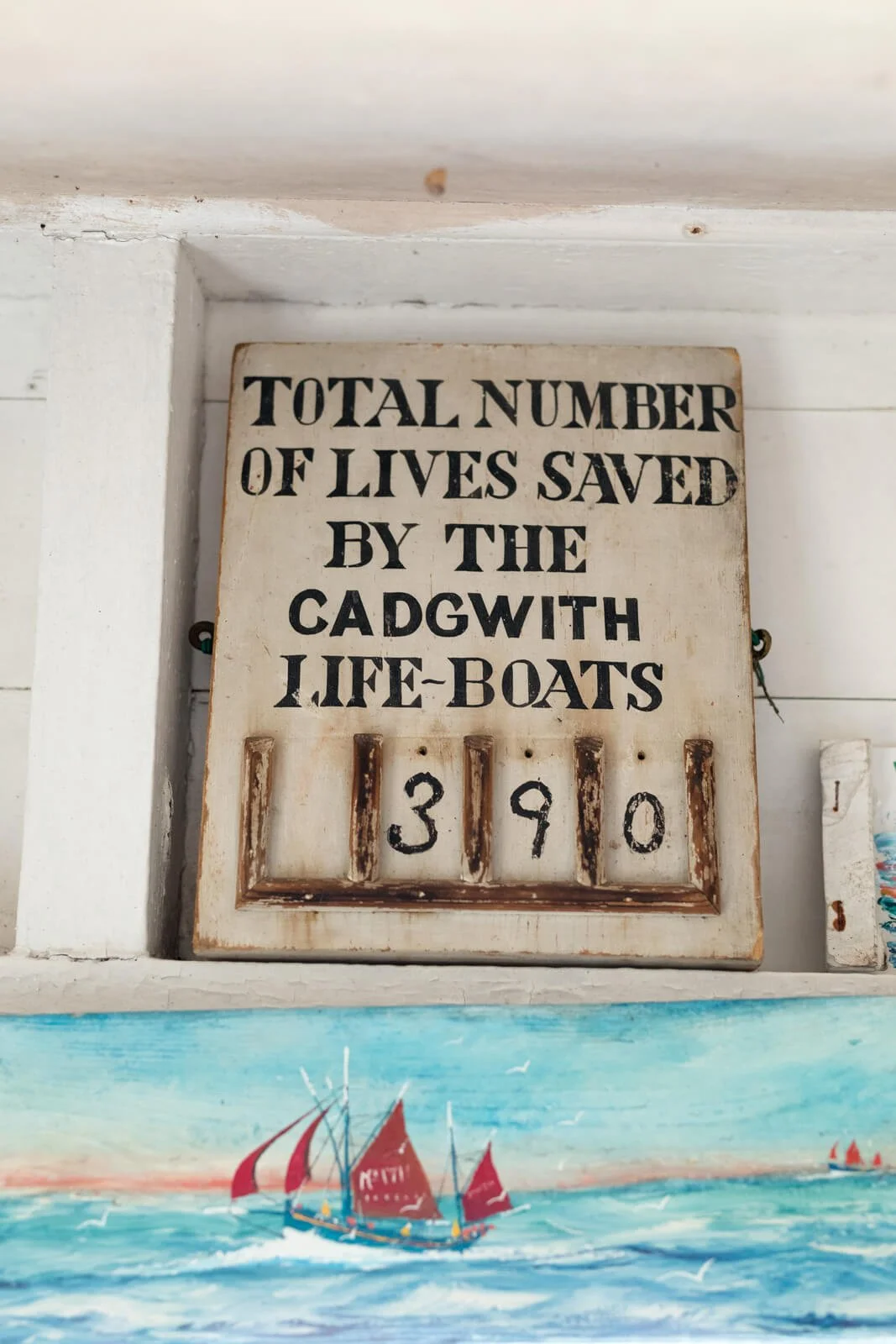 Sign showing "Total Number of Lives Saved by the Cadgwith Life-Boats: 390" with a nautical painting below.