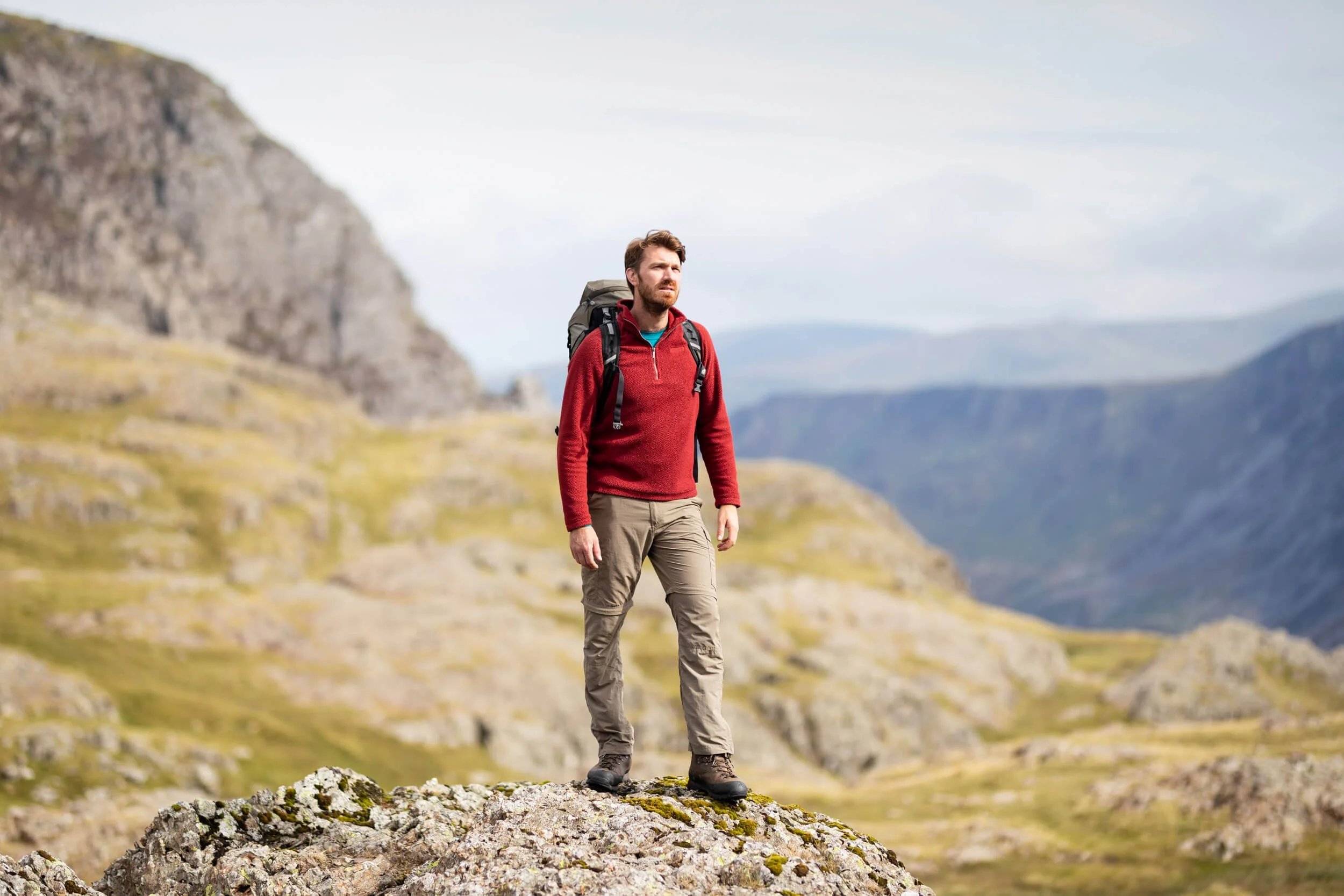 A man wearing a red sweater and backpack is hiking on a rocky mountain landscape.