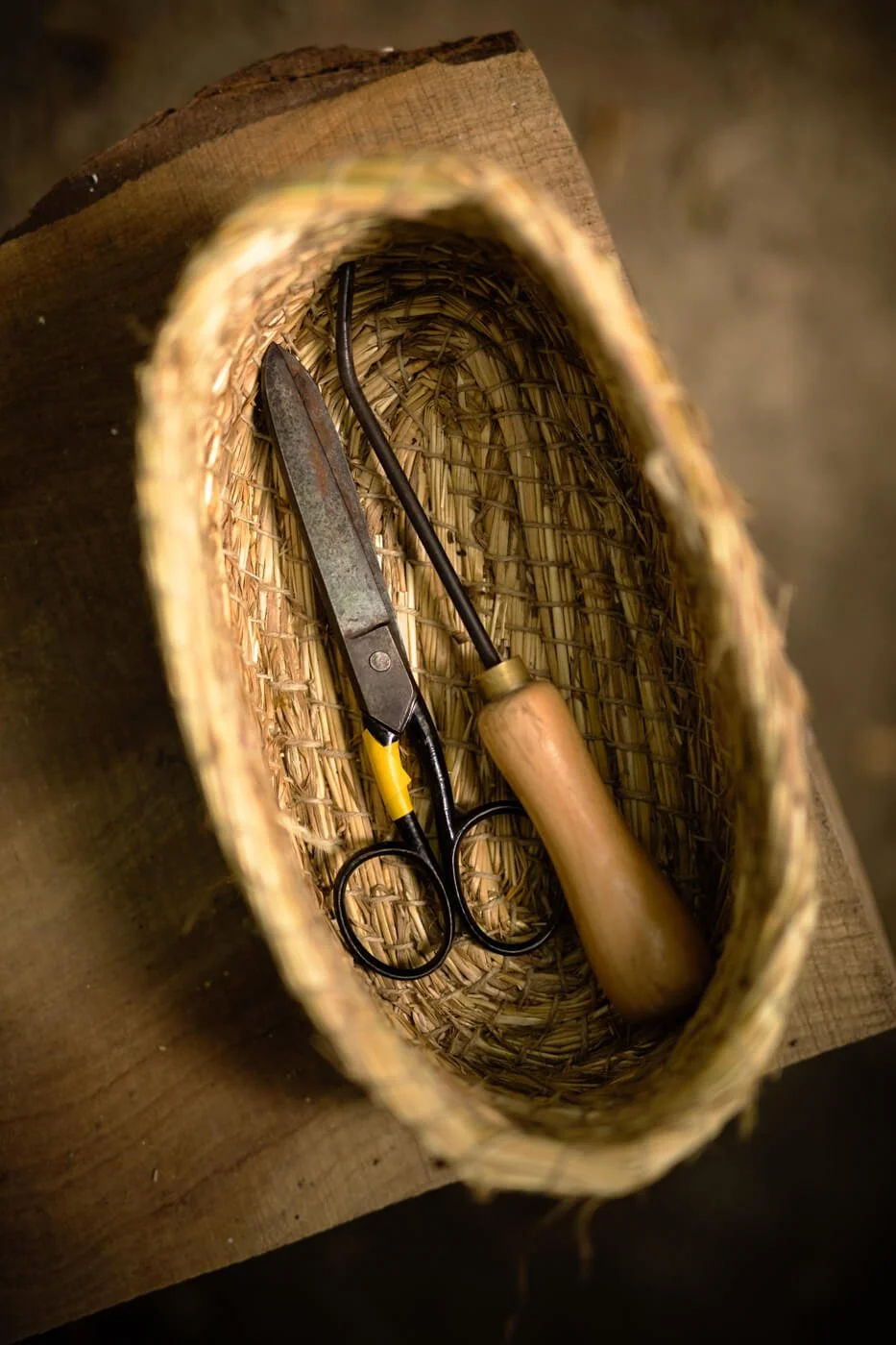 Close-up of a wicker basket containing scissors and a wooden-handled tool.